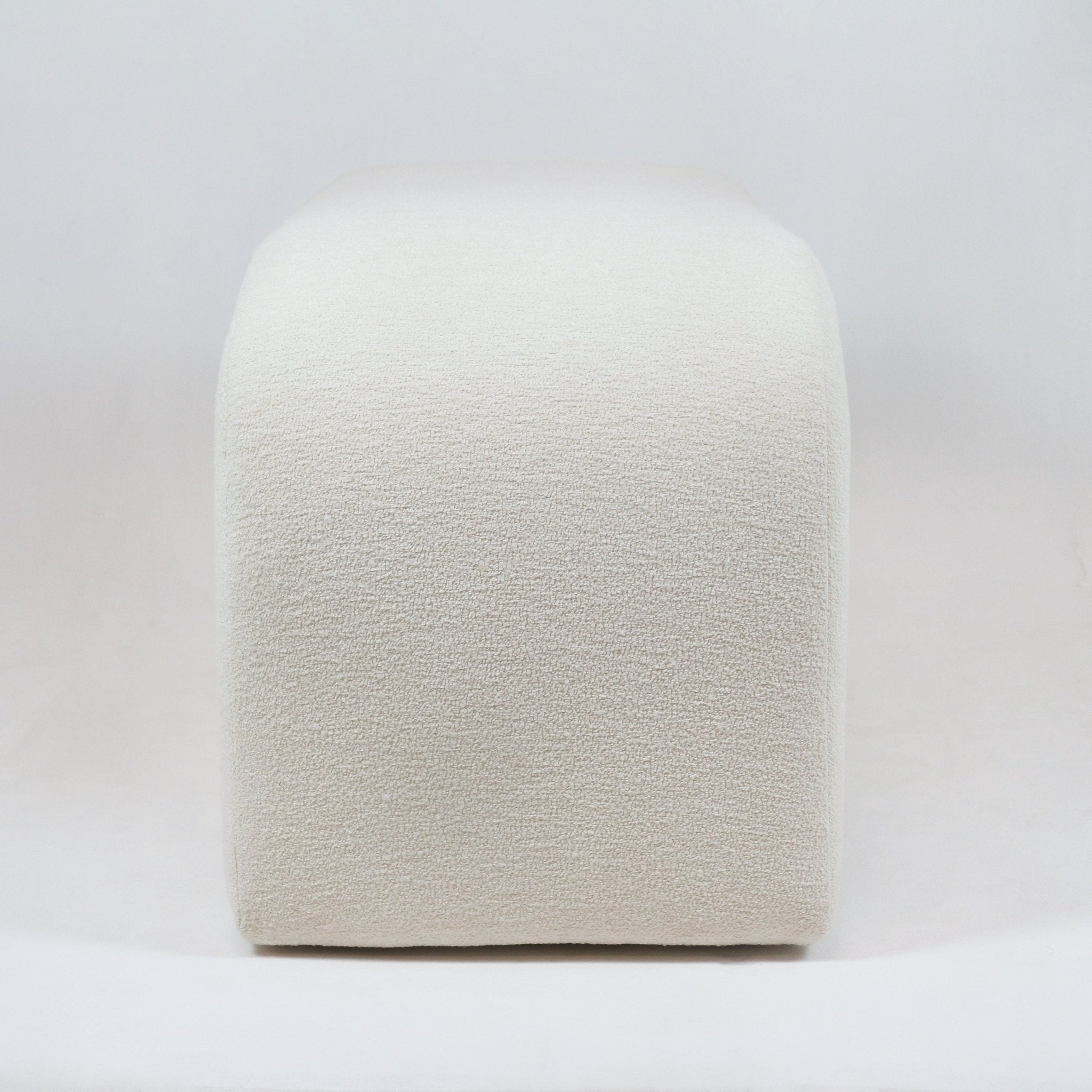 Front view of a backless end-of-bed bench upholstered in cream boucle fabric, showing rounded corners and a low, minimalist coastal-modern silhouette on a white background.