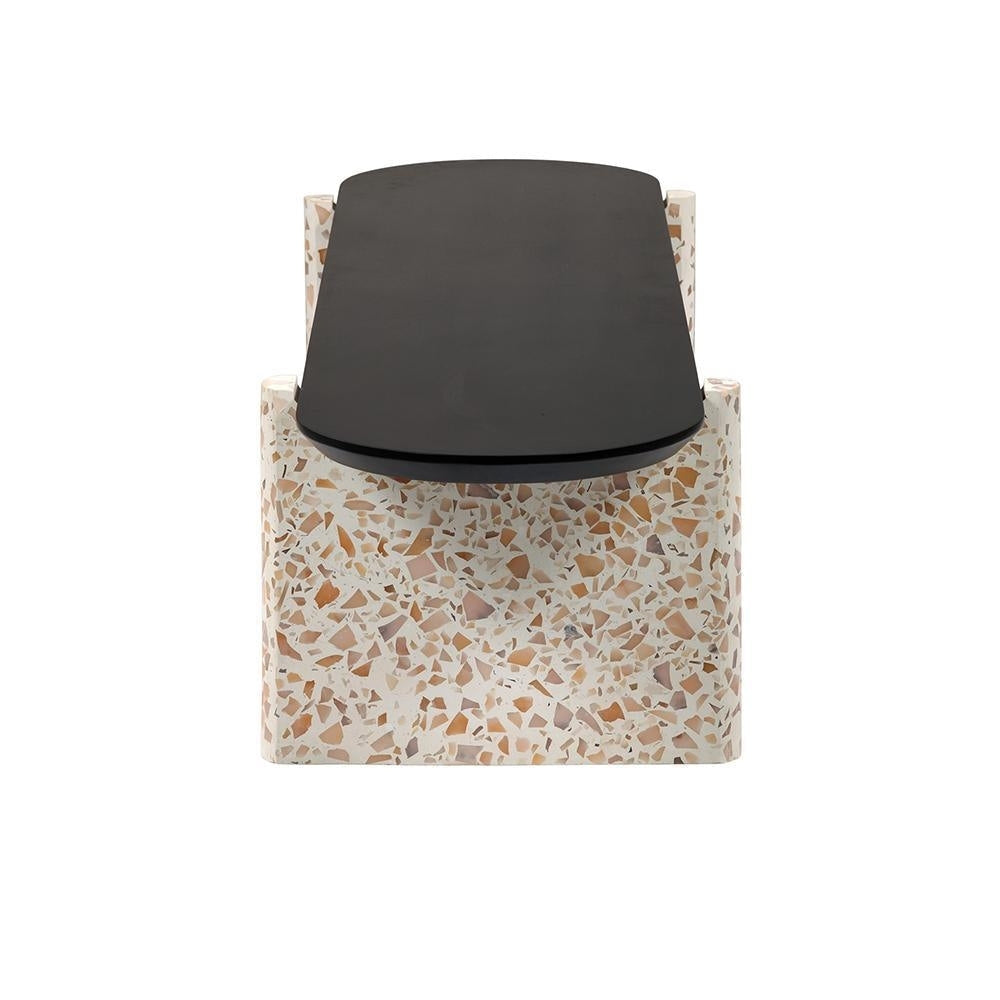 Front view of a modern coffee table with a black mahogany oval wood top mounted on a cream terrazzo block base patterned with tan and brown stone chips.