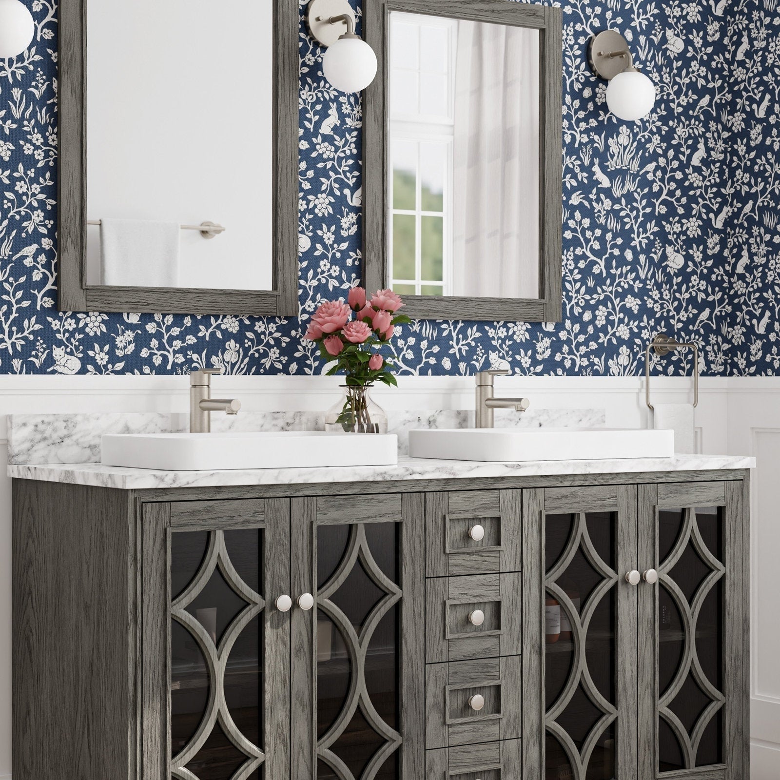 Freestanding gray solid-wood double bathroom vanity with marble-look stone countertop, two white rectangular vessel sinks and brushed-nickel faucets, decorative glass-front cabinet doors, framed mirrors and blue floral wallpaper.