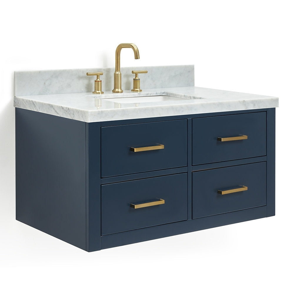 Wall-mounted modern solid wood bathroom vanity with navy cabinet, white stone marble top and integrated undermount sink, shown with brushed brass faucet and matching brass drawer pulls.
