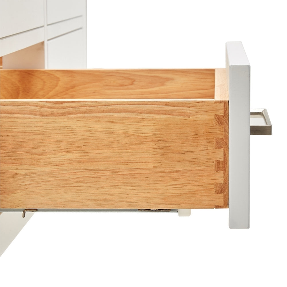 Close-up of a solid wood vanity drawer showing dovetail joints and natural wood grain interior, with a white painted drawer front, visible metal slide and a brushed-nickel rectangular handle.