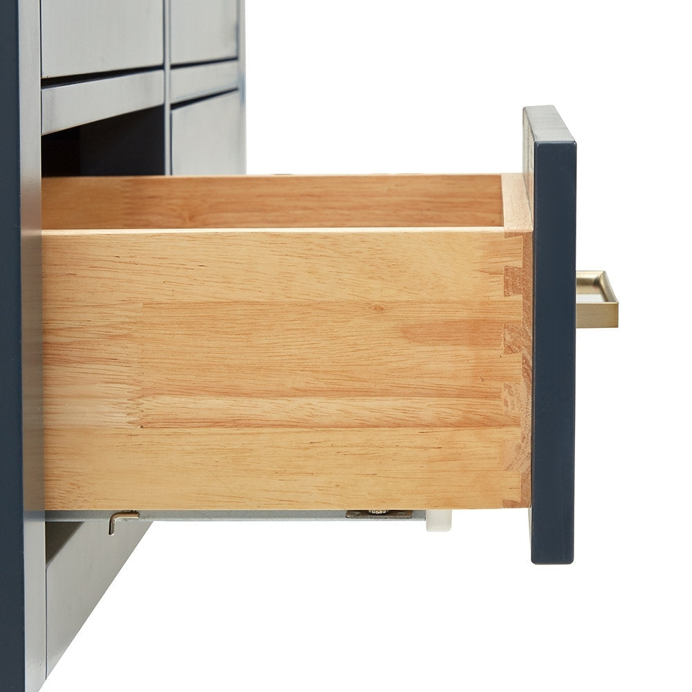 Close-up of a partially open solid wood vanity drawer showing a natural wood interior with dovetail joinery, stone-colored drawer face, brass-tone rectangular pull and visible metal slide hardware.