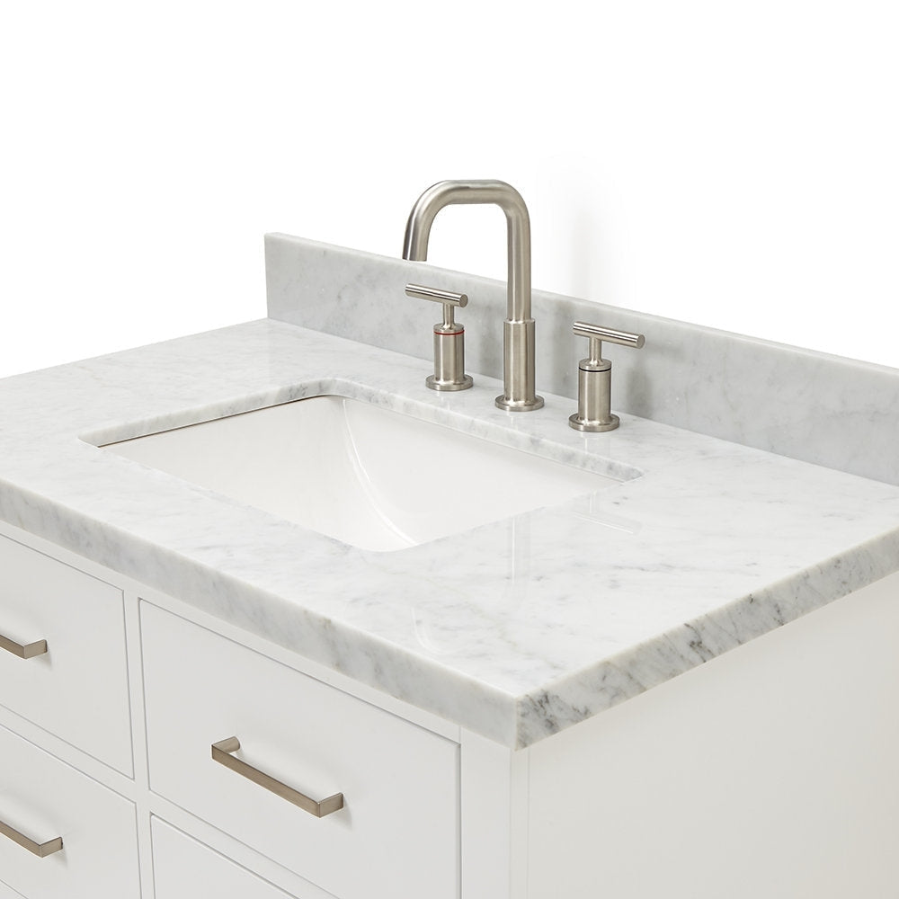Close-up of a modern white solid wood bathroom vanity with a marble stone countertop, integrated rectangular undermount ceramic sink, low stone backsplash and brushed-nickel three-piece faucet and matching drawer pulls.