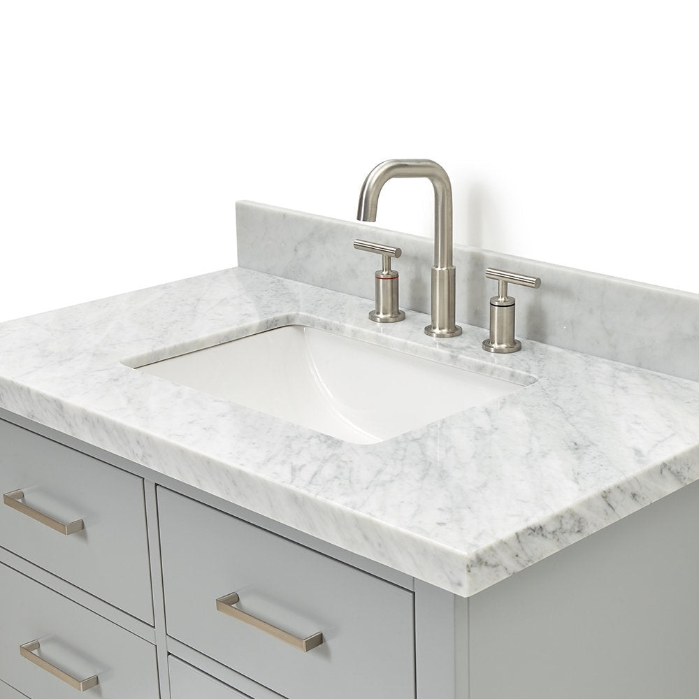 Modern gray solid wood vanity with a stone countertop and single undermount white ceramic sink, paired with a brushed nickel widespread faucet, matching metal drawer pulls, and a short stone backsplash.