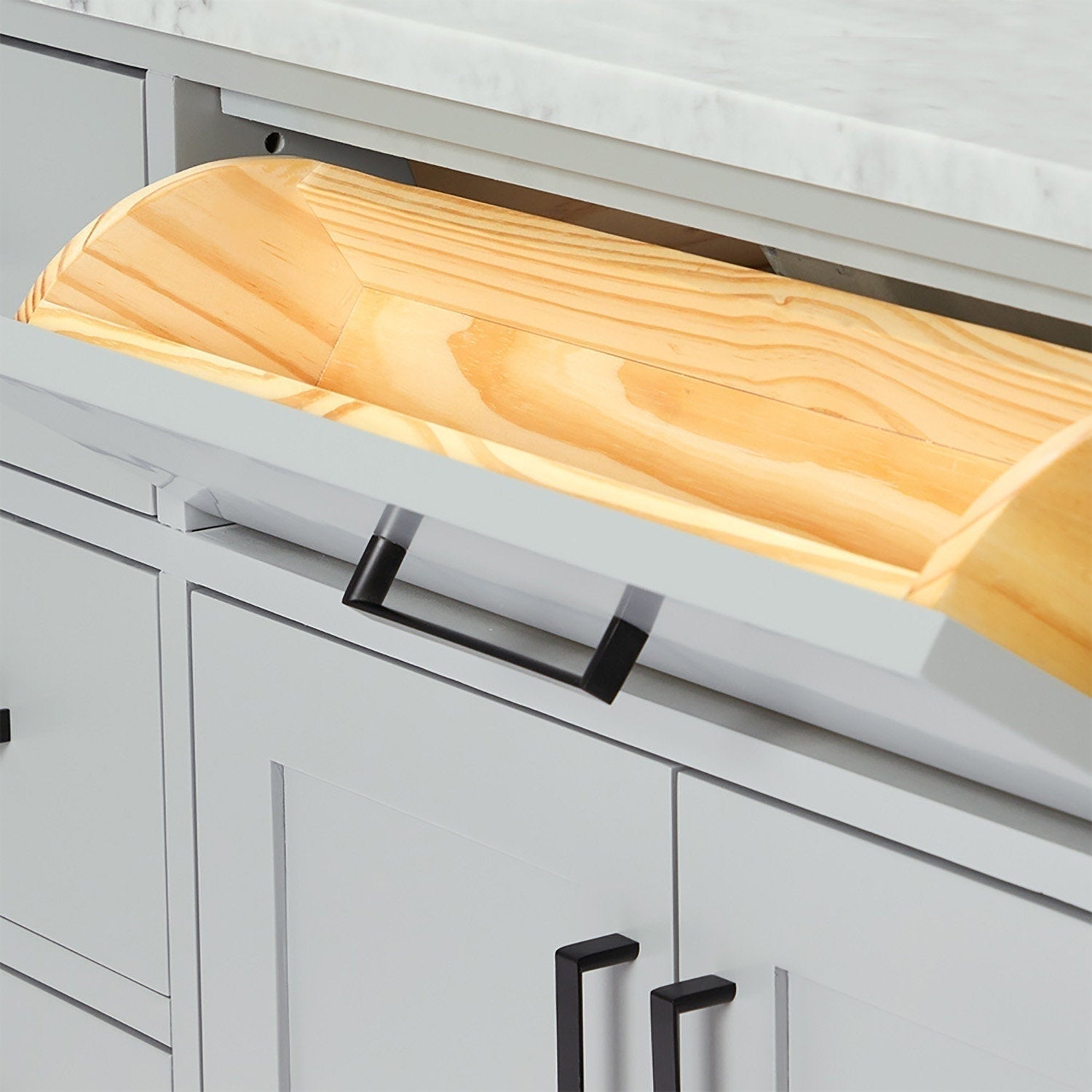 Close-up of an open gray modern bathroom vanity drawer revealing a light solid wood tray with visible natural grain beneath a stone countertop and matte black rectangular handles.