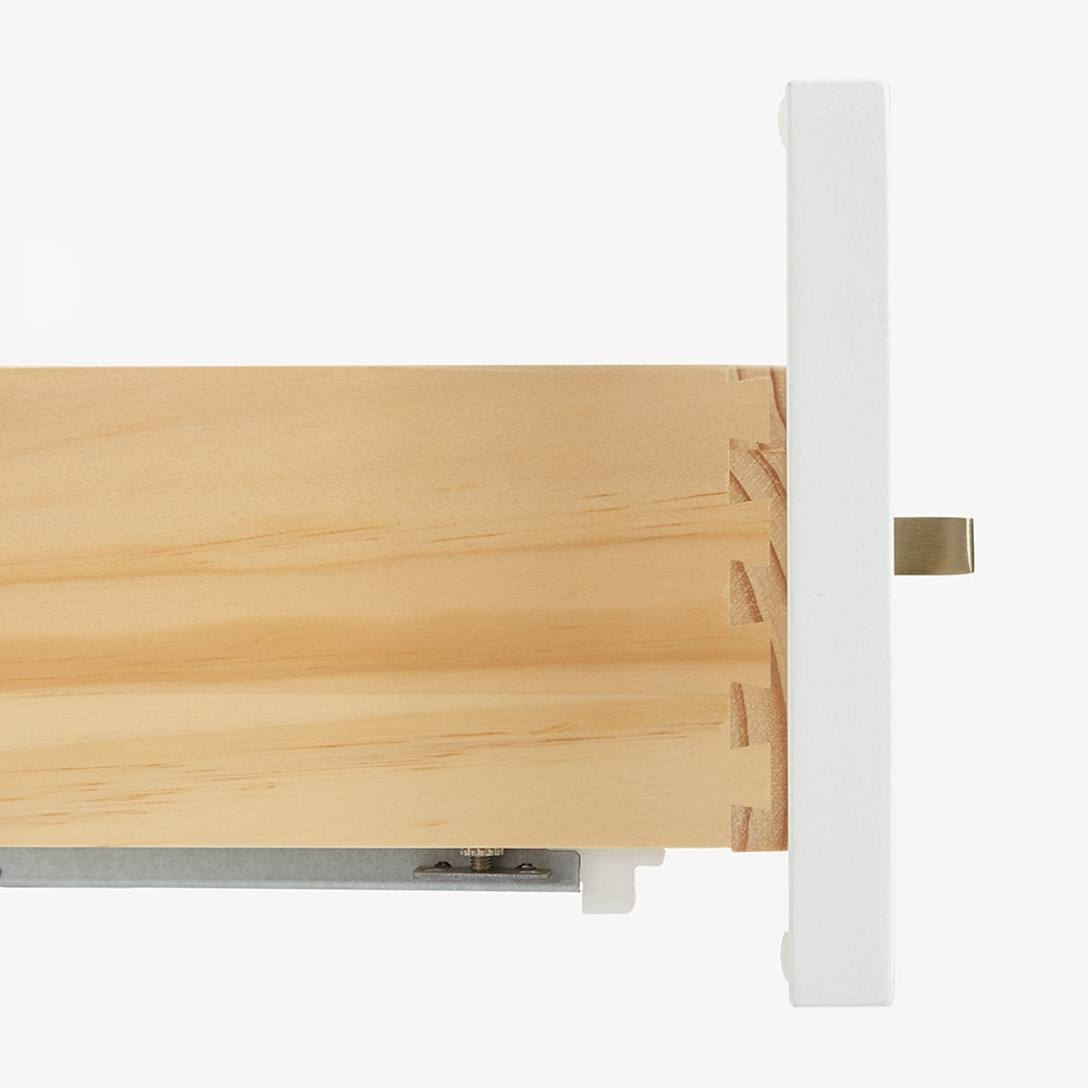 Close-up of a light solid wood drawer side showing dovetail joinery attached to a white painted drawer front, with metal drawer slide and satin bronze pull tab visible.