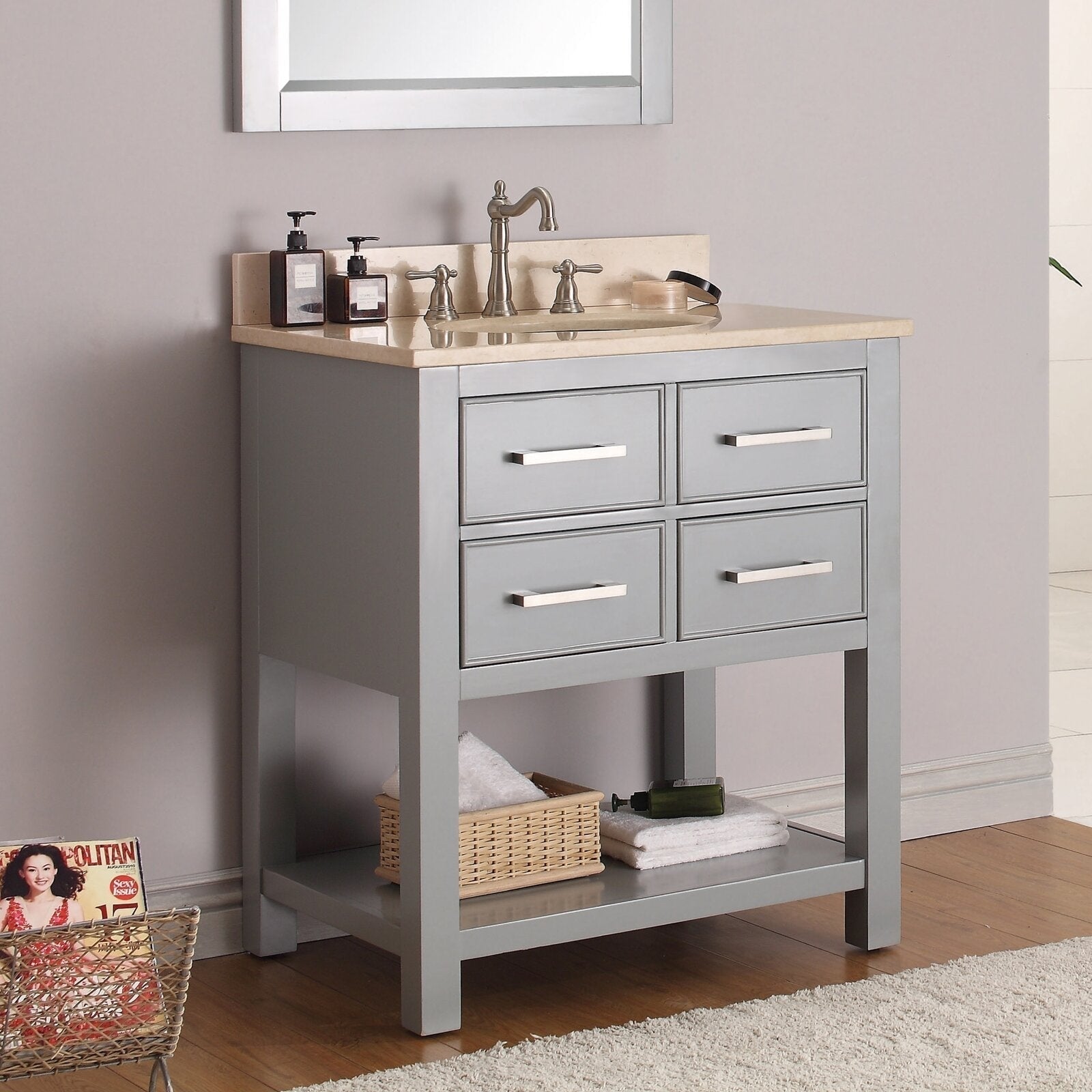 Freestanding modern gray solid-wood bathroom vanity with a stone top and integrated ceramic sink, brushed-nickel faucet, four drawers with metal bar pulls and an open lower shelf holding towels and a wicker basket.
