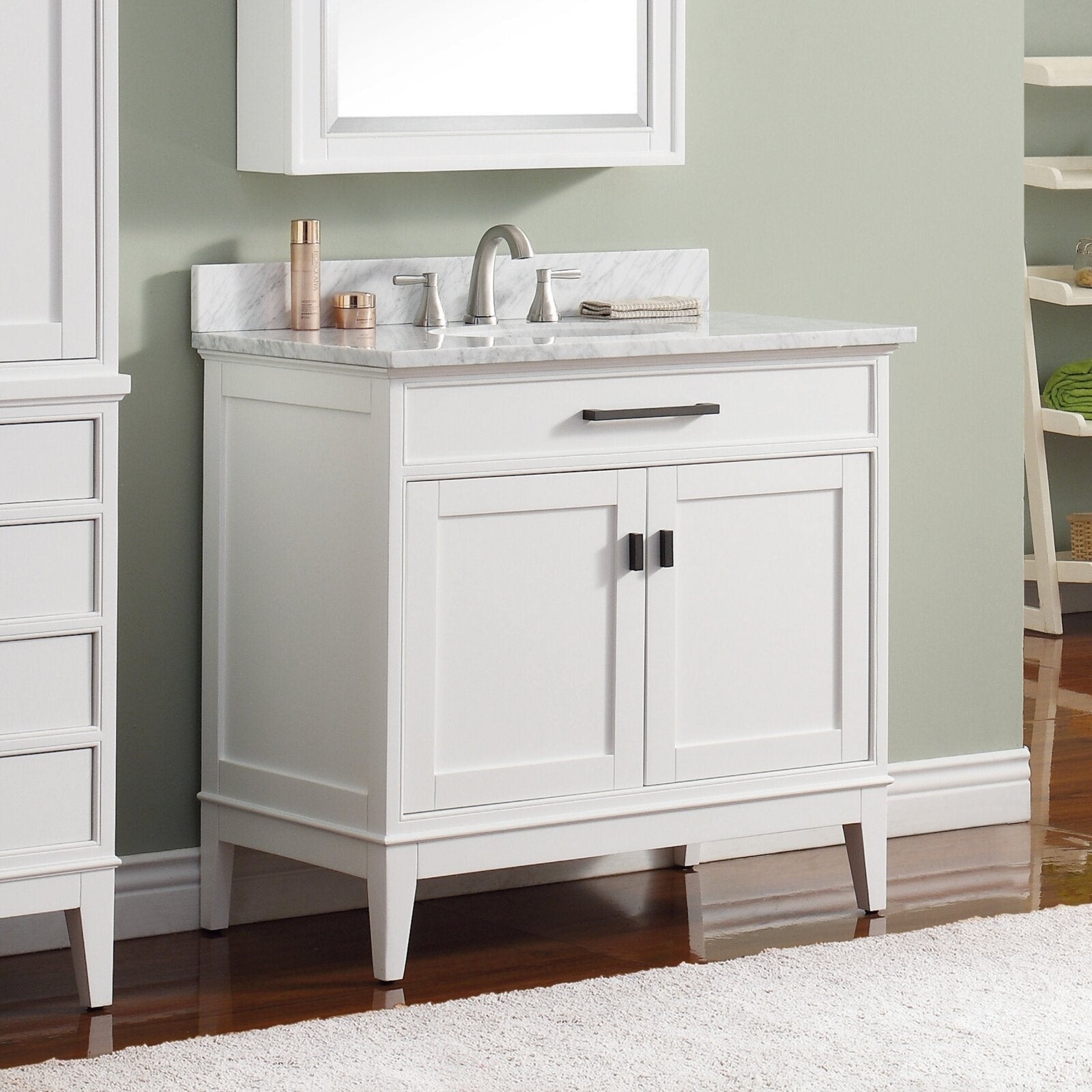Modern freestanding white solid-wood bathroom vanity with a stone marble countertop, single undermount sink, brushed nickel faucet, top drawer and two cabinet doors with dark metal pulls on tapered legs.