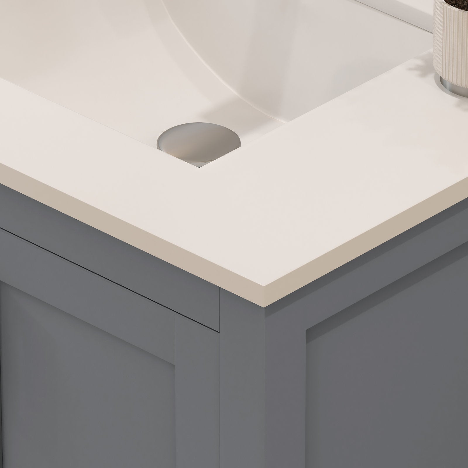 Close-up of a modern 30-inch bathroom vanity corner featuring a stone-colored top with integrated white sink, round metal drain cover, and a gray solid-wood contemporary cabinet with flat-panel door.
