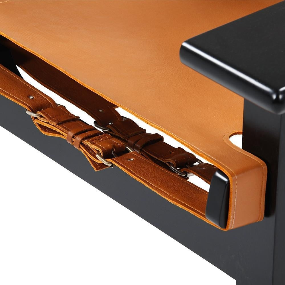 Close-up of a tan leather sling seat with buckled brown leather straps attached to a black mahogany solid wood frame and armrest.