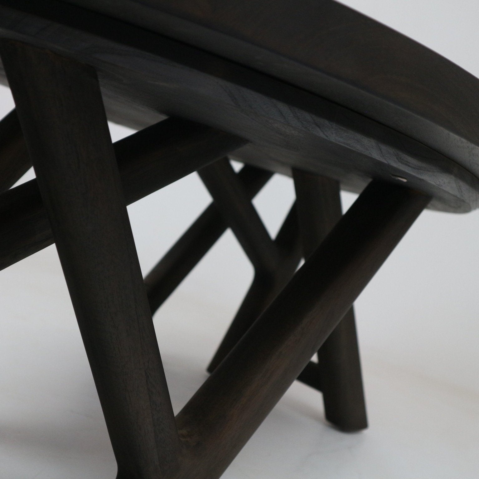 Close-up of the underside of a modern mahogany coffee table in a smoked-black finish, showing solid wood crossed legs and the rounded tabletop edge.