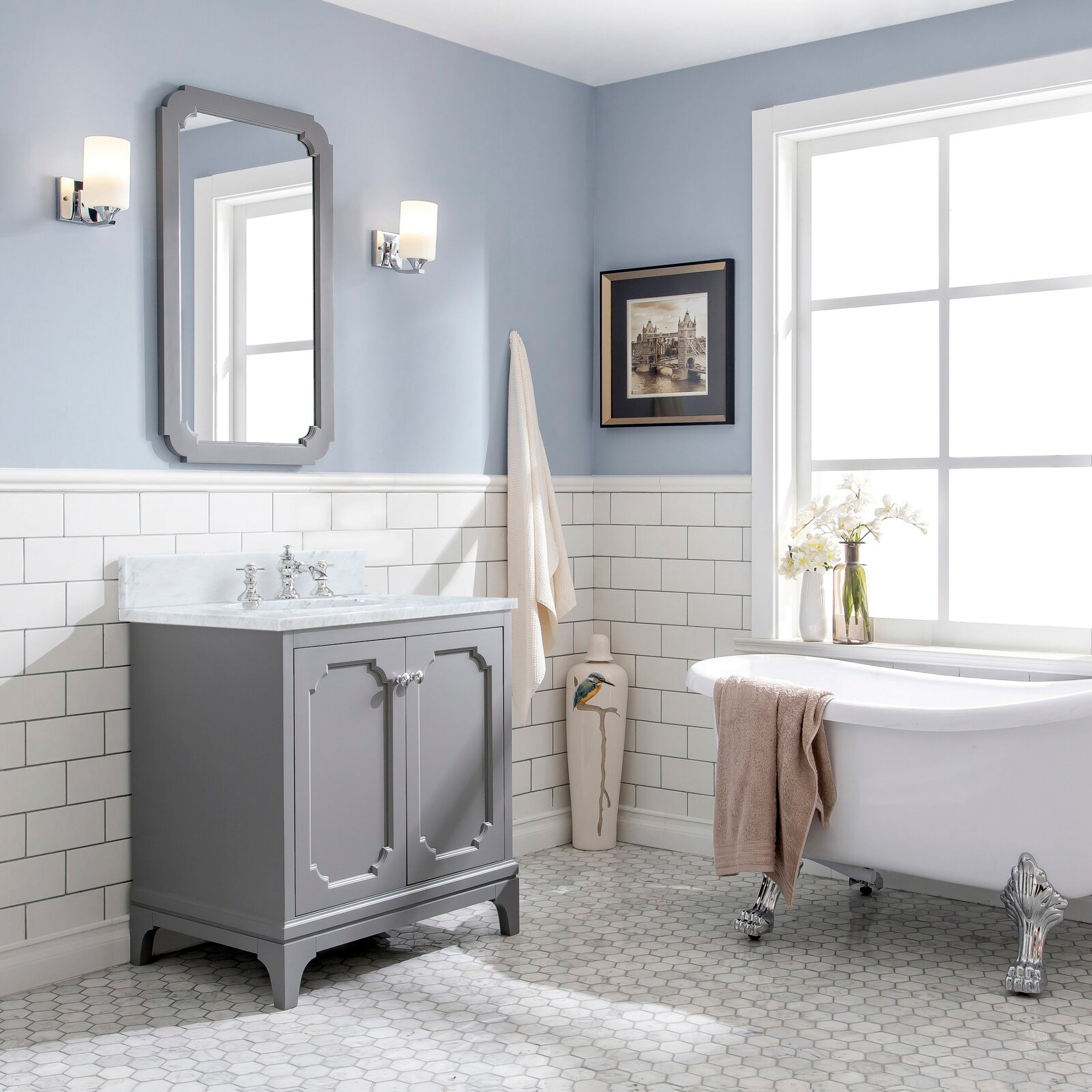 Freestanding modern gray solid-wood single-sink vanity with Carrara white marble countertop and chrome faucet, framed mirror and wall sconces above, subway tile wainscot and clawfoot tub on hex marble floor.