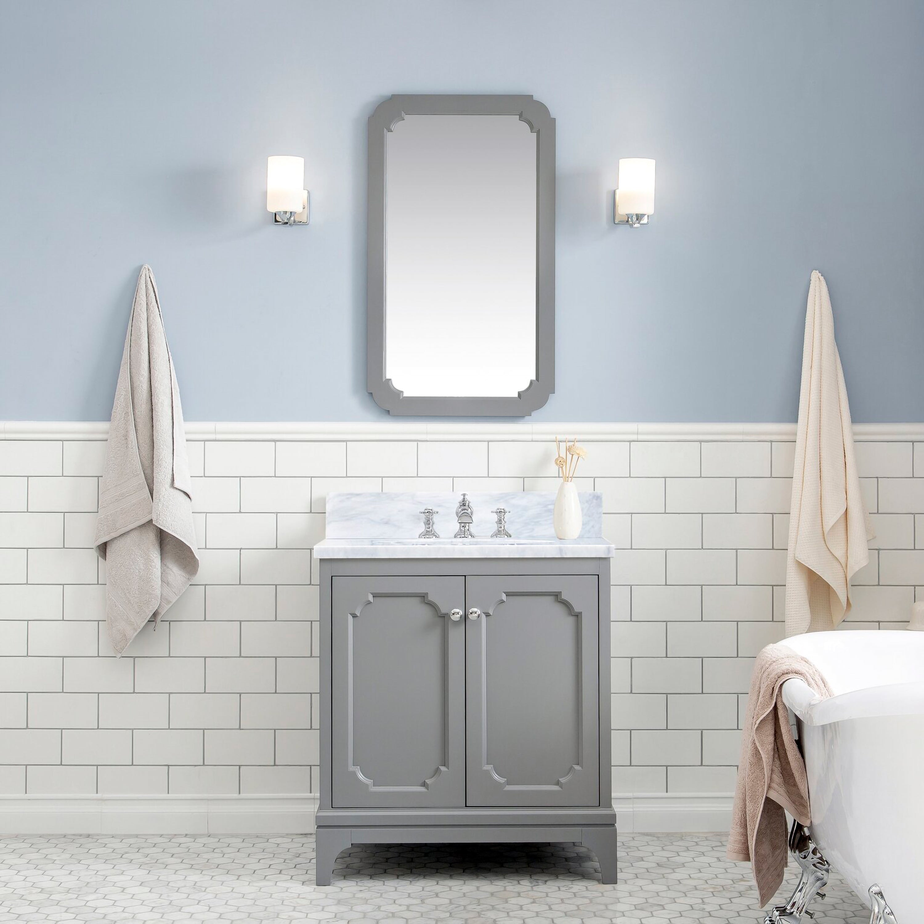 Contemporary gray solid-wood single-sink vanity with Carrara white marble countertop and chrome faucet, gray framed mirror above, subway tile wainscot, wall sconces, hanging towels and a partial clawfoot tub view.