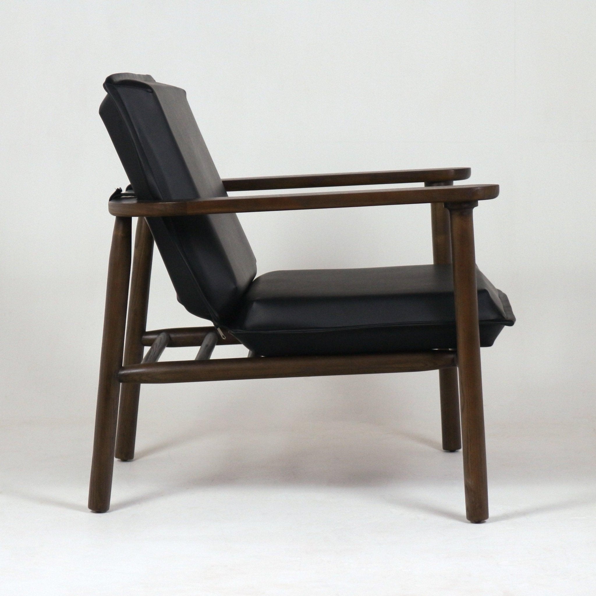 Side view of a midcentury modern lounge chair with black faux-leather seat and back cushions on a dark walnut solid wood frame, low arms, and exposed horizontal support slats.