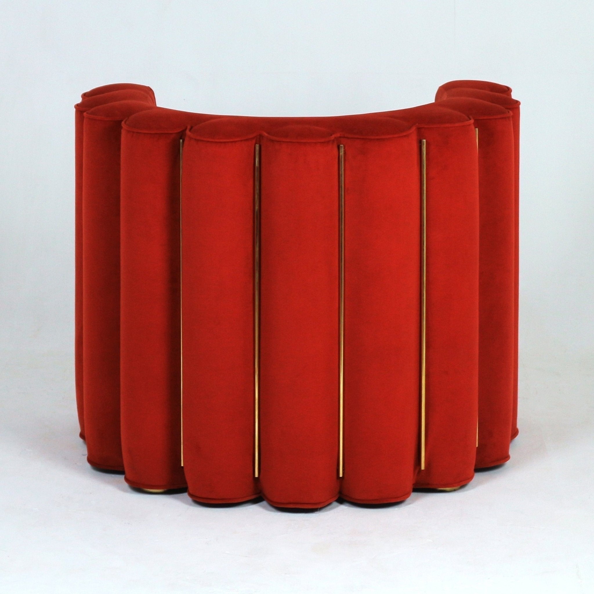 Rear view of a semi-circular modern accent chair upholstered in red velvet with vertical scalloped channels separated by slim gold metal rods, shown against a plain white background.