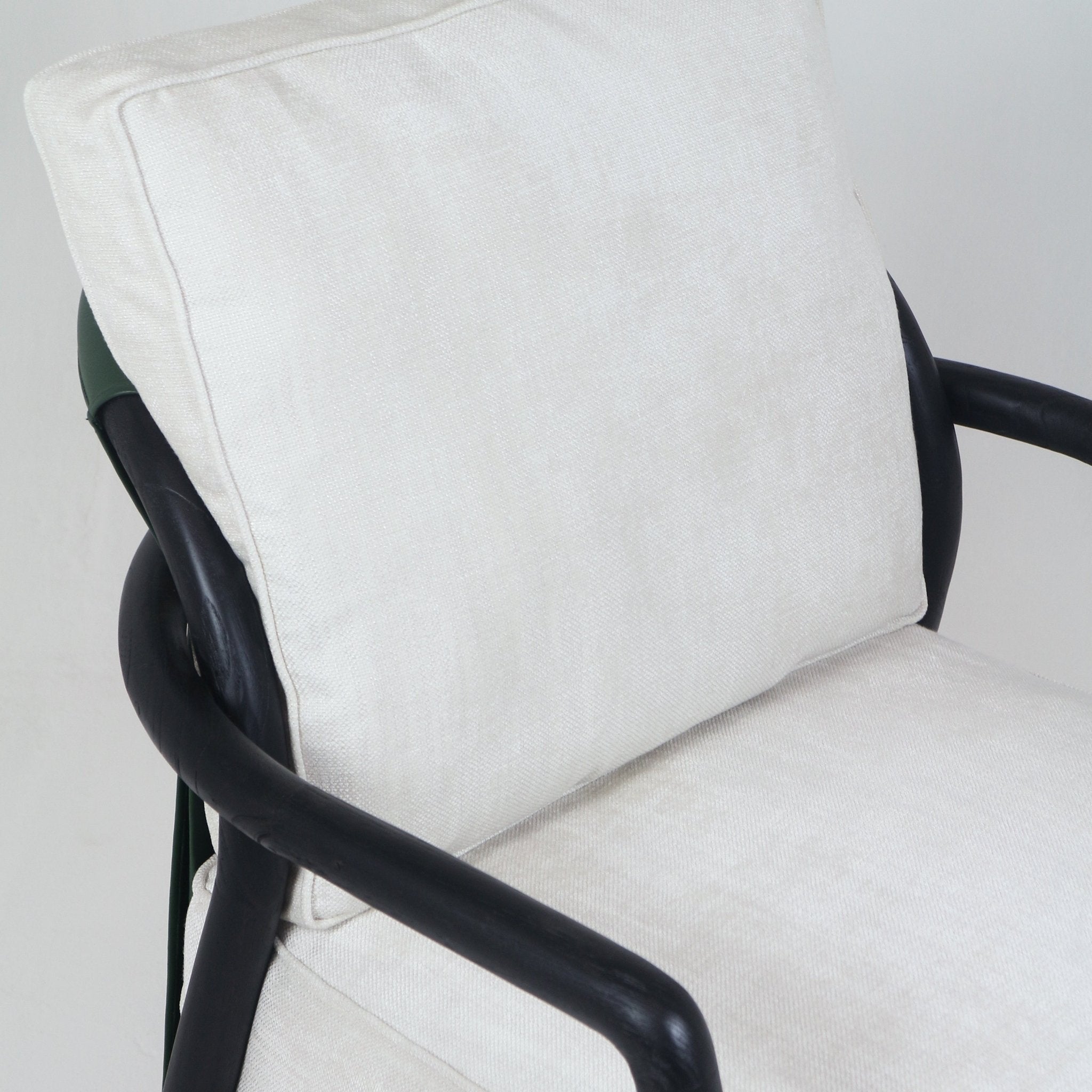 Close-up of a mid-century modern armchair showing cream fabric seat and back cushions with piped edges and a curved dark-finished teak arm frame.