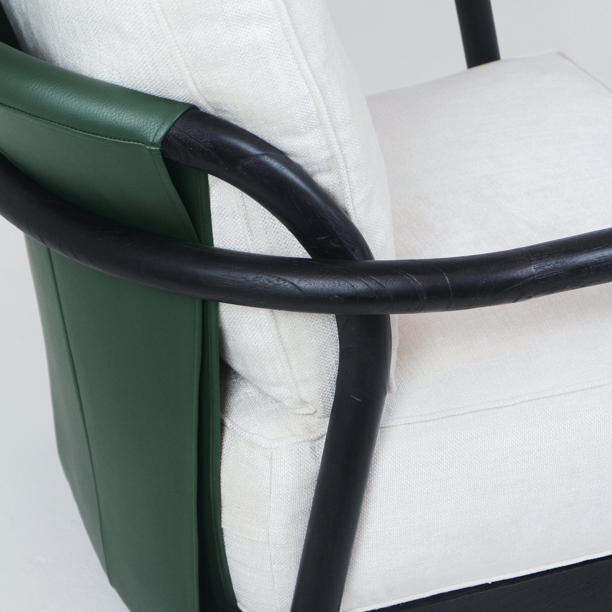 Close-up of a mid-century modern armchair showing a curved dark teak wood arm, green leather side panel and cream fabric seat cushion with visible stitching.