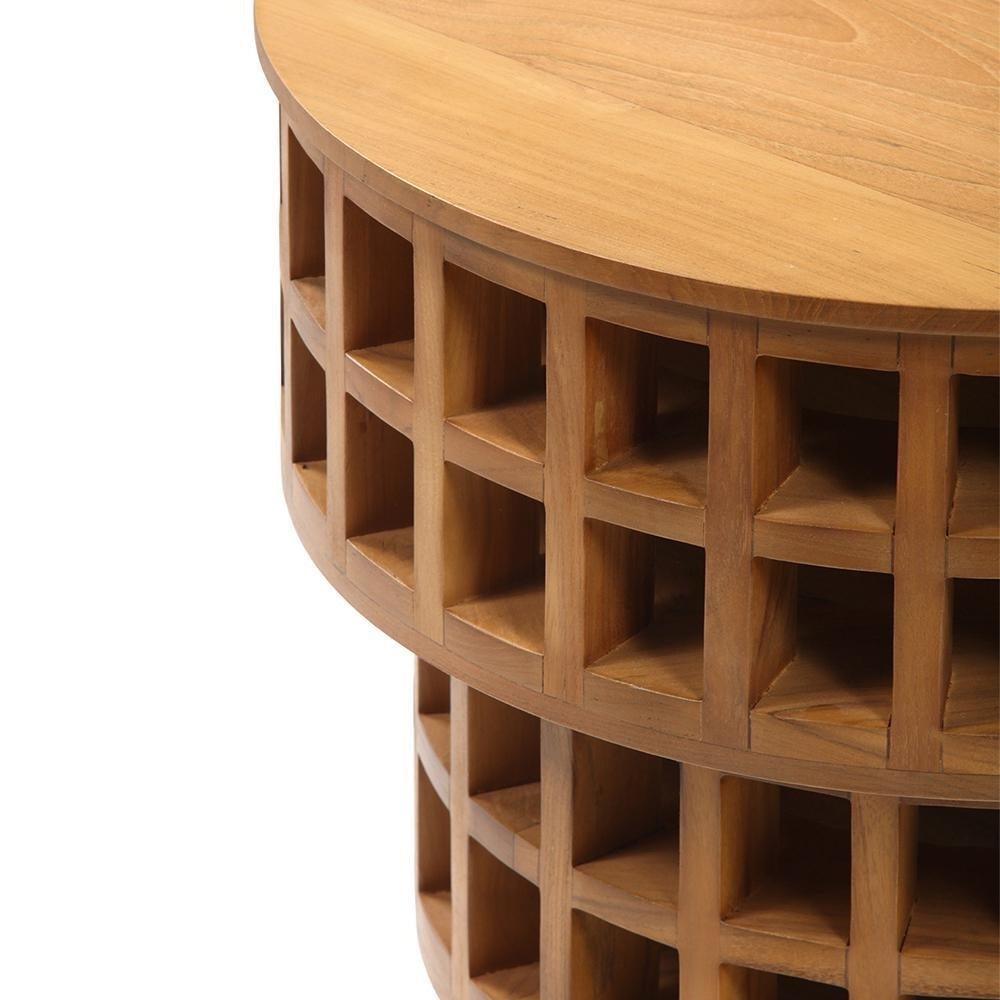 Close-up of a round mid-century modern solid teak side table showing a smooth teak top and stacked lattice-grid open cubbies carved into the cylindrical base.