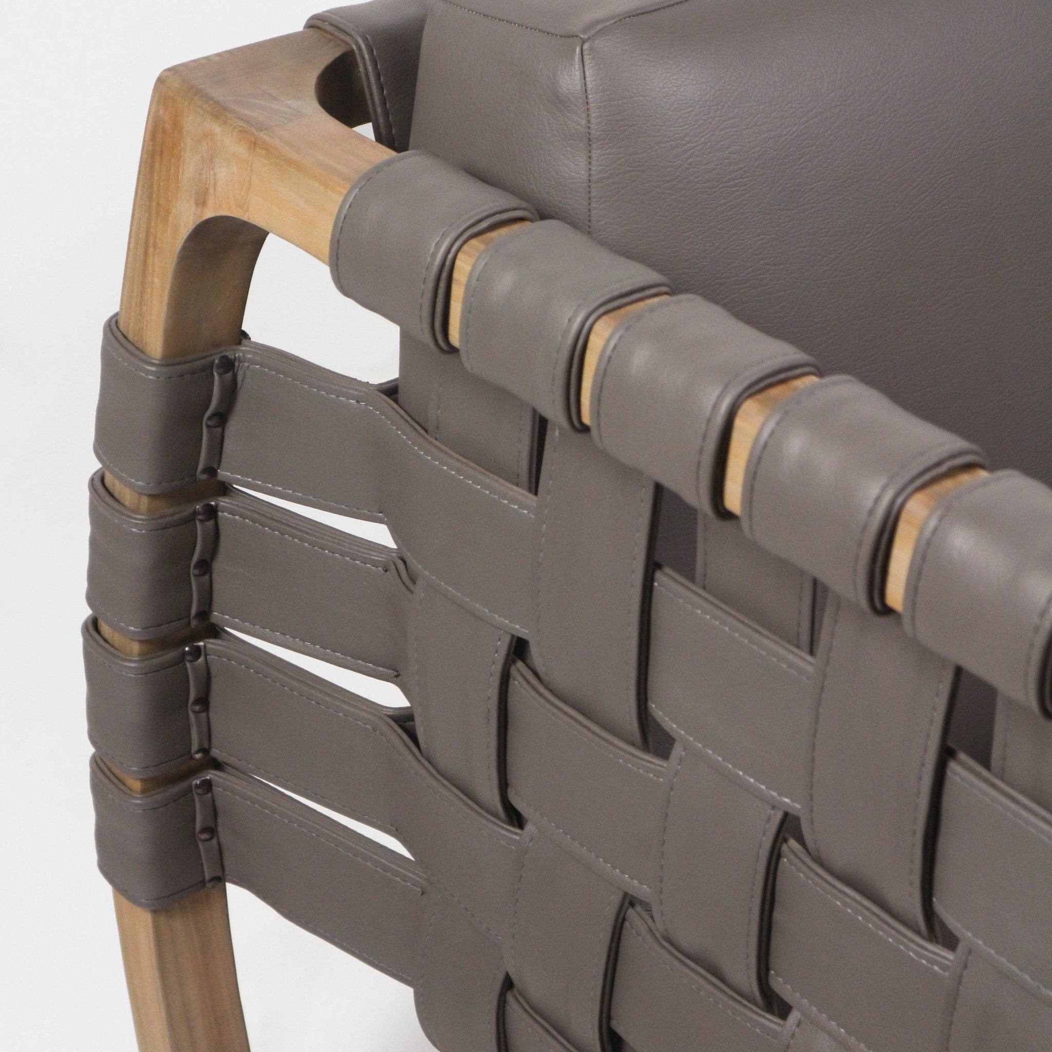Close-up of a modern lounge chair showing taupe faux-leather straps woven into a webbed back and wrapped around a natural solid wood arm, with visible stitching and dark metal rivets securing the straps.