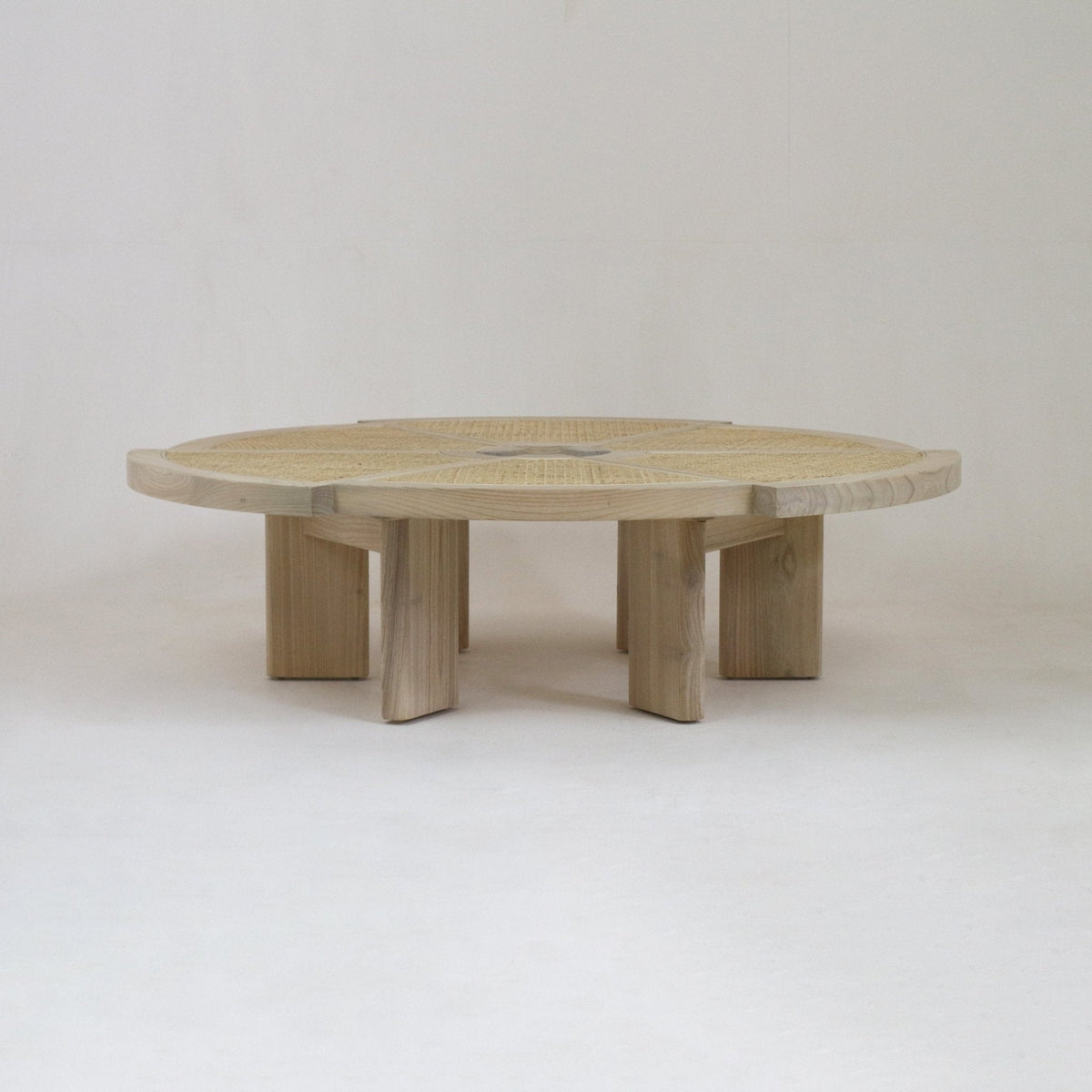 Low round coffee table in natural blonde oak with a woven cane inset top and chunky segmented pedestal legs, photographed on a simple neutral background.