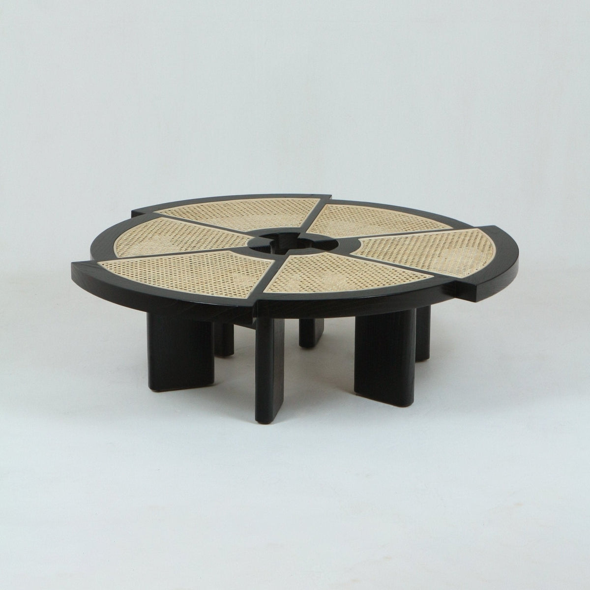 Low round modern coffee table with a black stained solid-wood frame and six natural cane-woven wedge panels in the tabletop, featuring a central circular cutout and short rectangular slab legs.