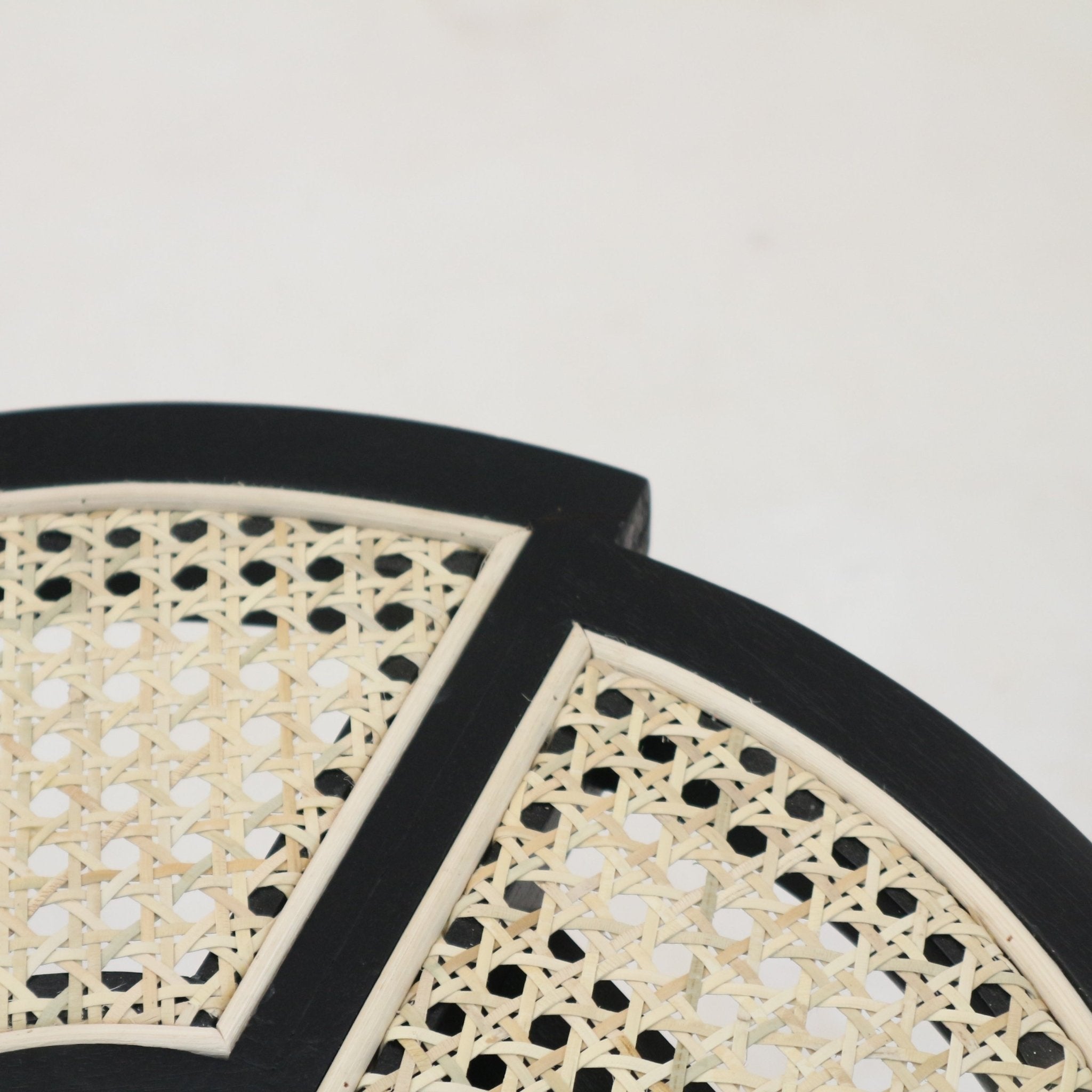 Close-up of a black-gloss solid wood side table top featuring a natural cane rattan weave set into a segmented frame with light wood trim.