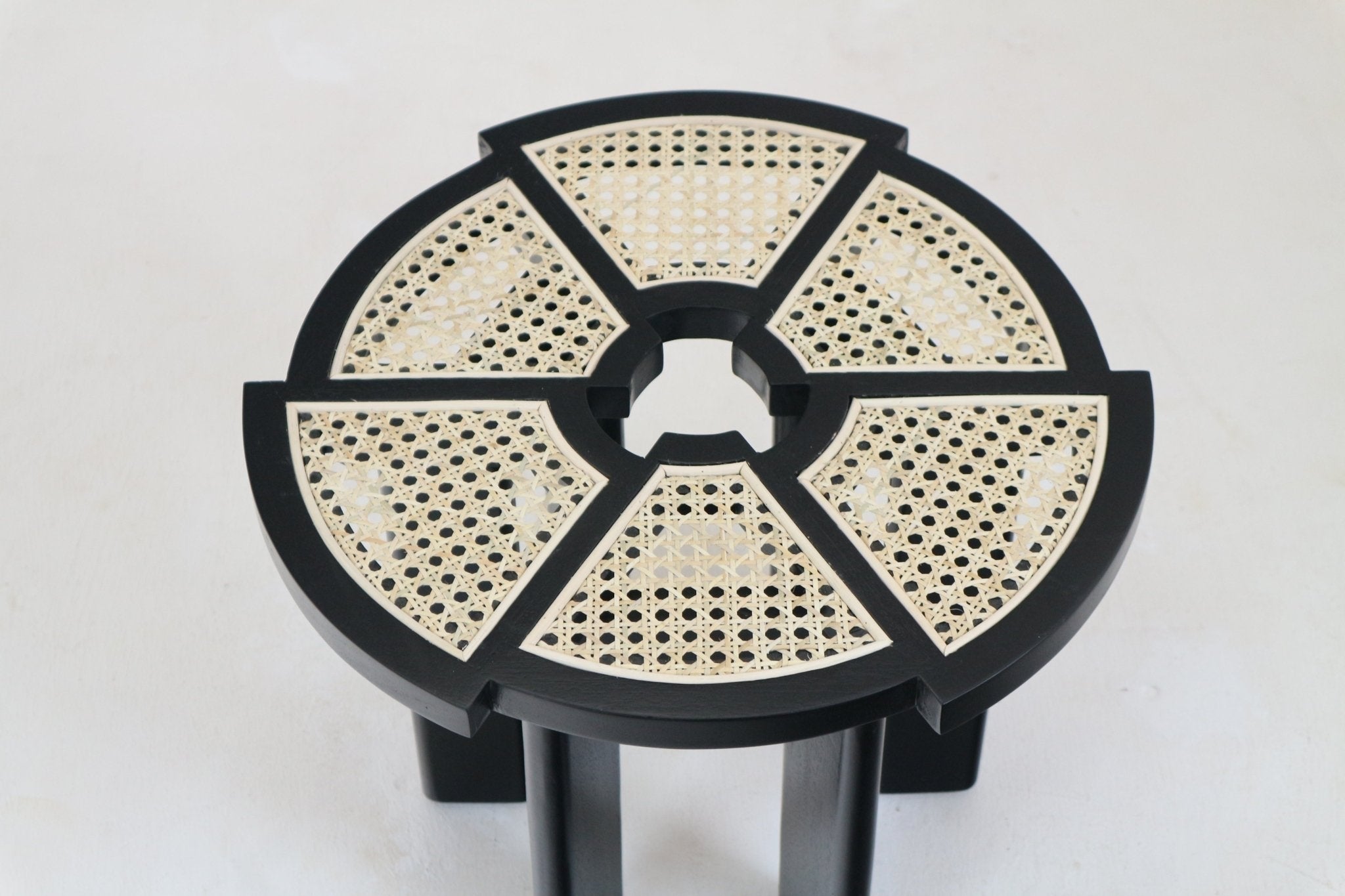 Top-down view of a round black-gloss solid wood side table with six natural cane rattan insets arranged around a central circular opening, supported by black wood legs.