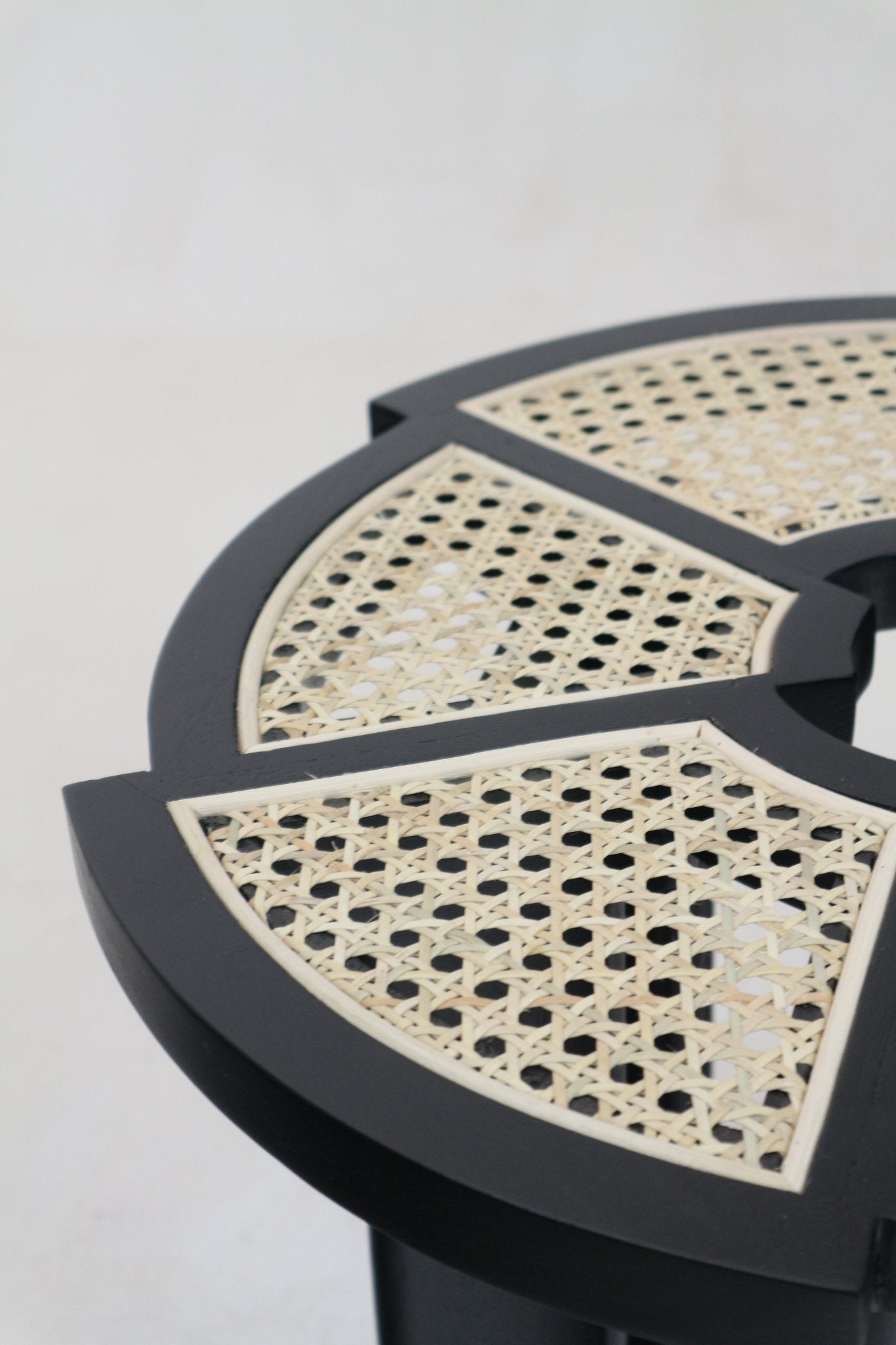 Close-up of a black gloss round side table top with segmented natural cane rattan insets set into a solid wood frame, highlighting the woven cane pattern and smooth black finish.