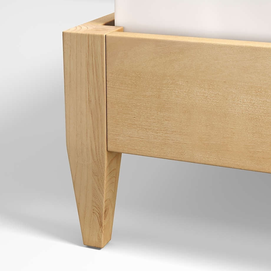 Close-up of a teak mid-century modern bed showing the tapered leg and side rail in a natural blonde wood finish, highlighting wood grain and clean joinery details.