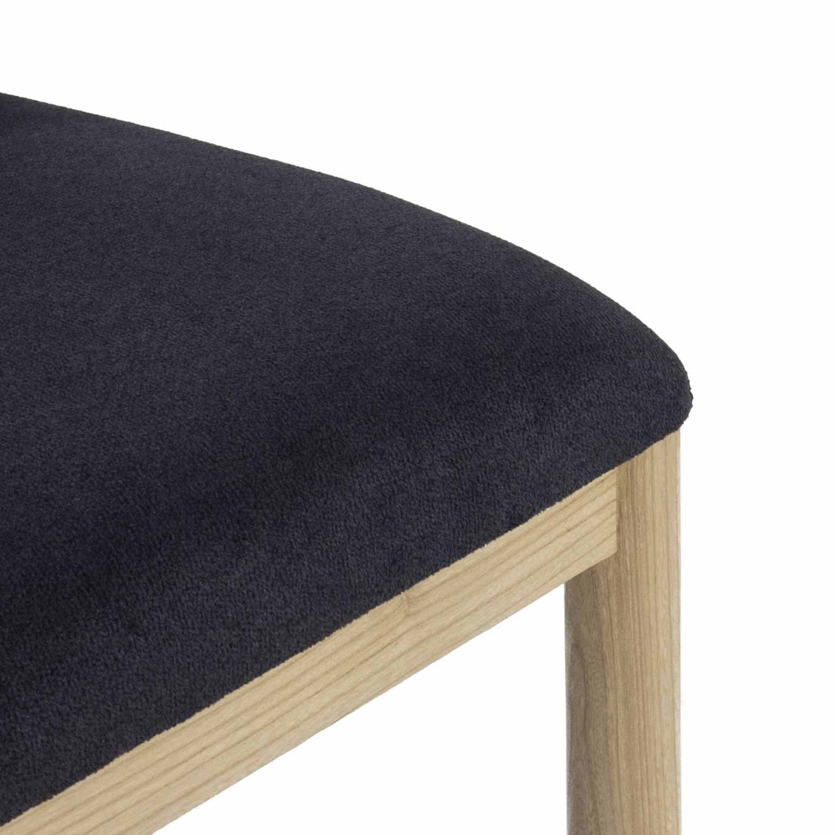Close-up of a charcoal bouclé upholstered stool seat with a rounded cushioned edge resting on a natural oak frame and visible oak leg.