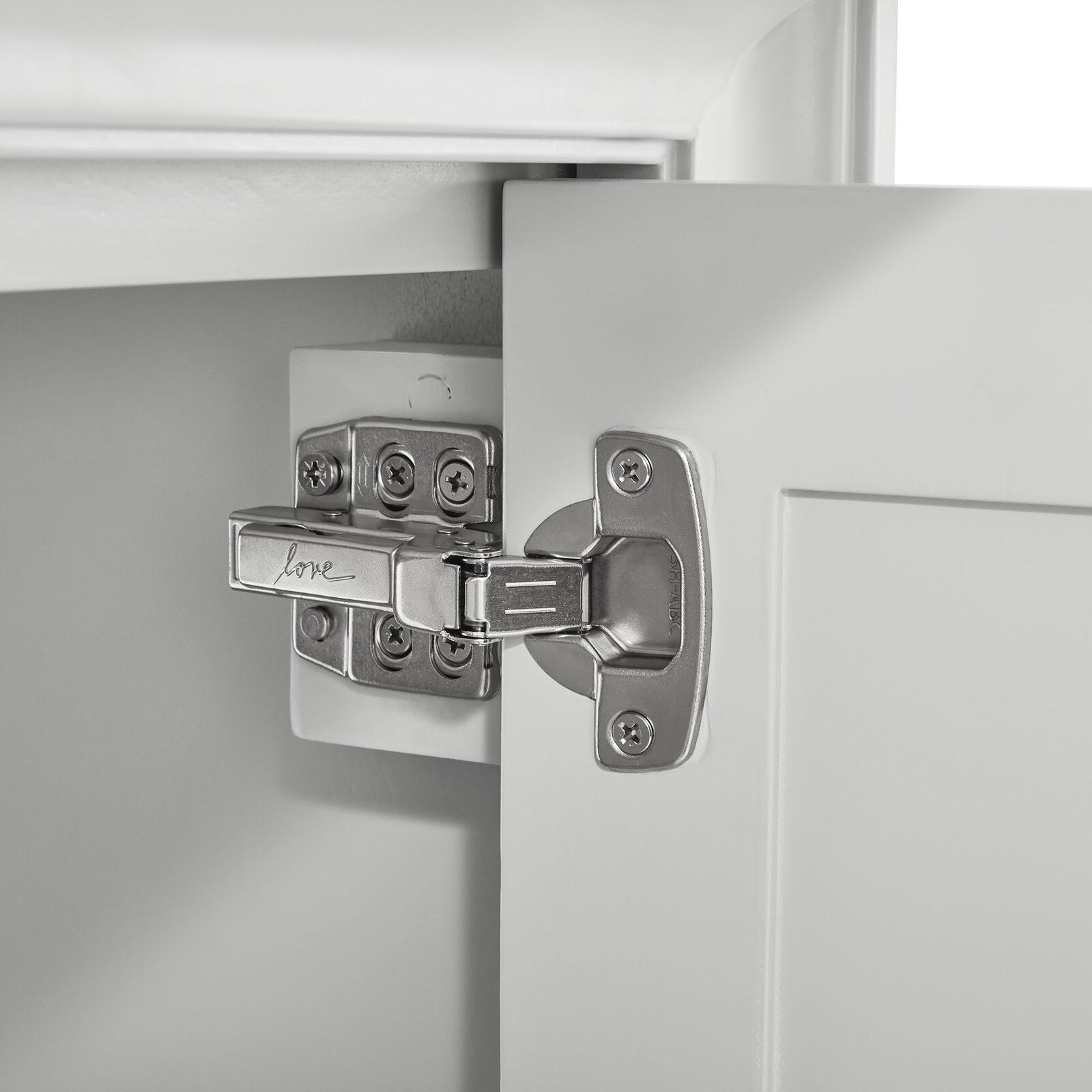 Close-up of a chrome soft-close cabinet hinge mounted to a white wooden bathroom vanity door and inner frame, showing screws, hinge cup and hardware details.