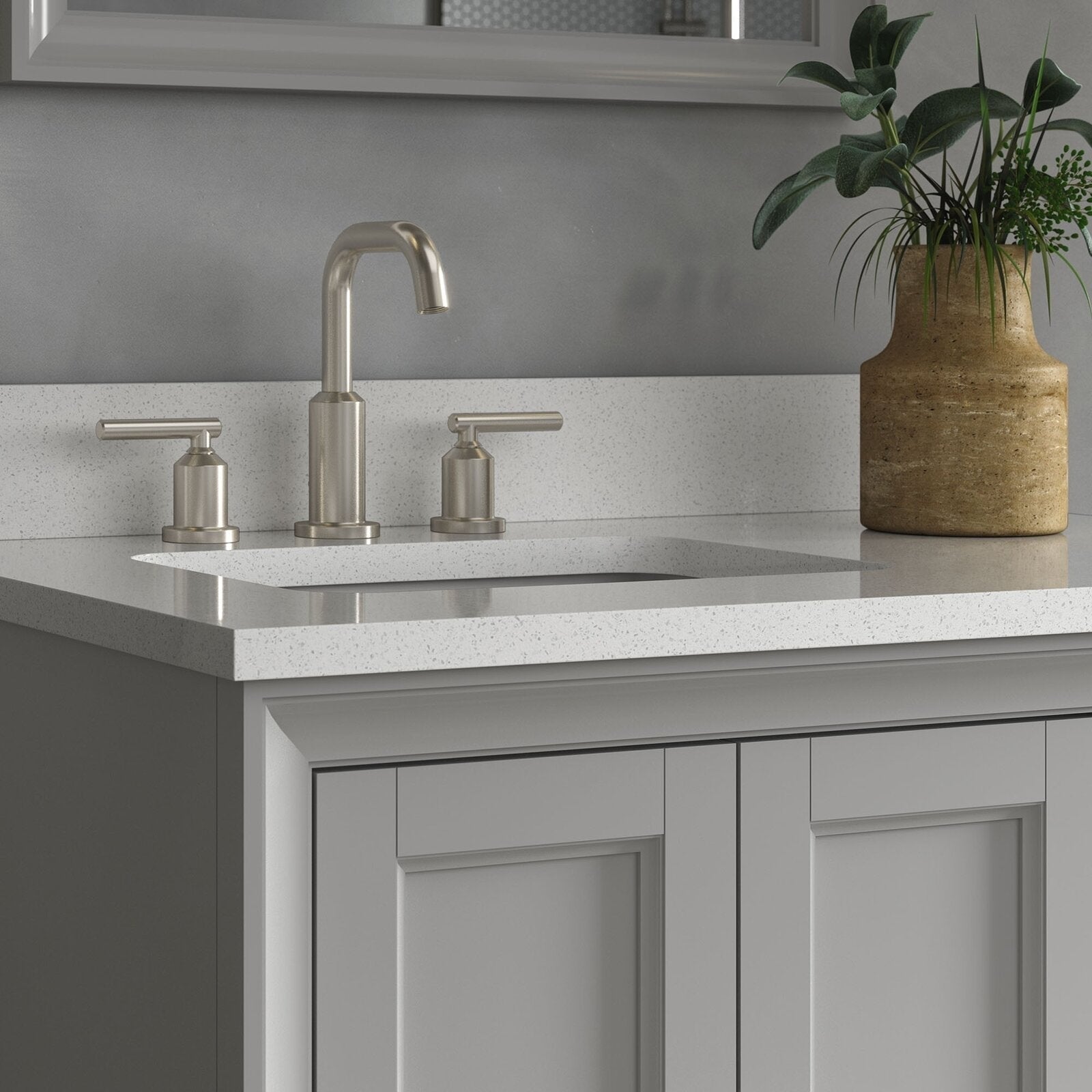 Close-up of a modern single-sink bathroom vanity with a stone speckled countertop, undermount ceramic sink, brushed nickel two-handle faucet and gray solid-wood shaker cabinet with a ceramic planter.