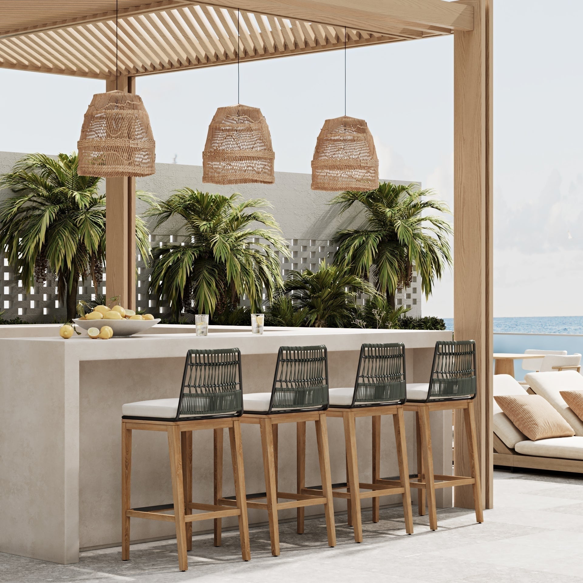 Four mid-century modern outdoor bar stools with teak legs, black woven rope backs and light fabric cushions lined at a concrete bar under a wooden pergola with wicker pendant lights and tropical plants, ocean visible beyond.
