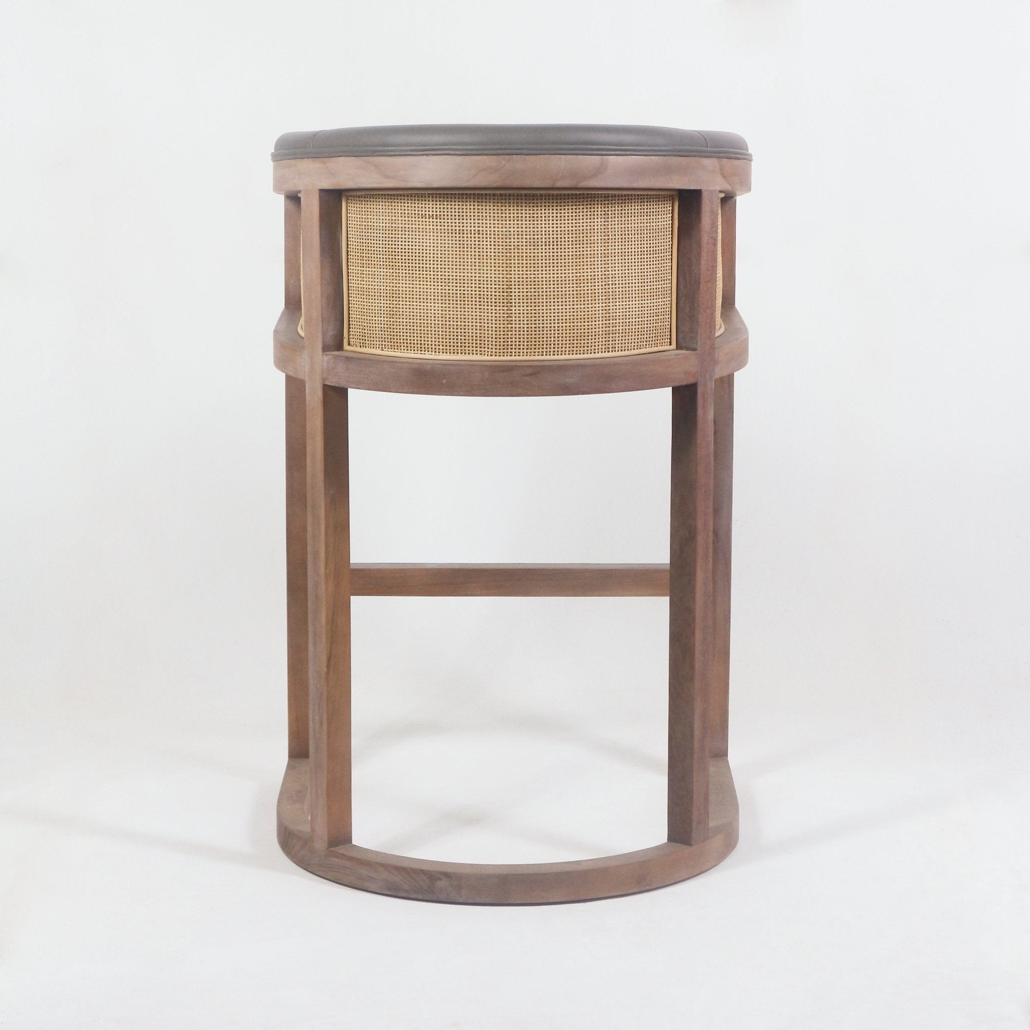 Rear view of a mid-century modern teak bar stool with a woven cane back panel, rounded natural wood frame and a dark faux-leather padded seat.