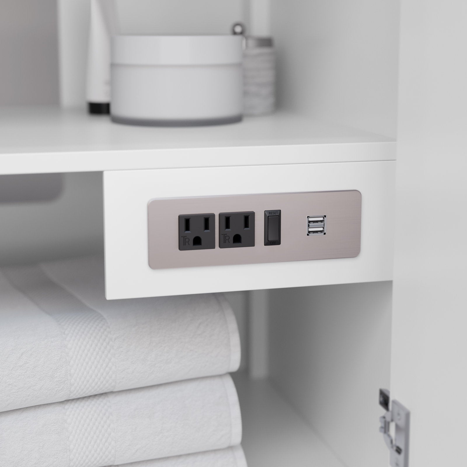Close-up of a built-in brushed-nickel power panel mounted inside a white solid wood bathroom vanity, showing two electrical outlets, a reset switch and dual USB ports above neatly folded white towels.
