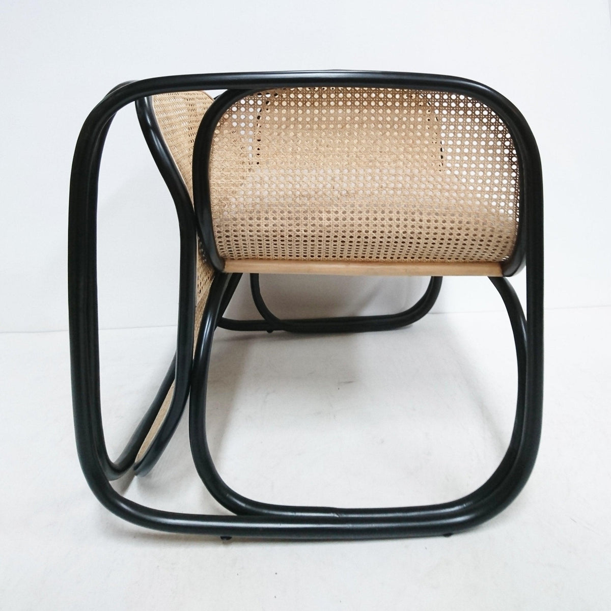 Low-angle view of a modern contemporary lounge chair with a curved black metal tubular frame and natural cane rattan seat and back, highlighting the looped base and woven cane pattern.