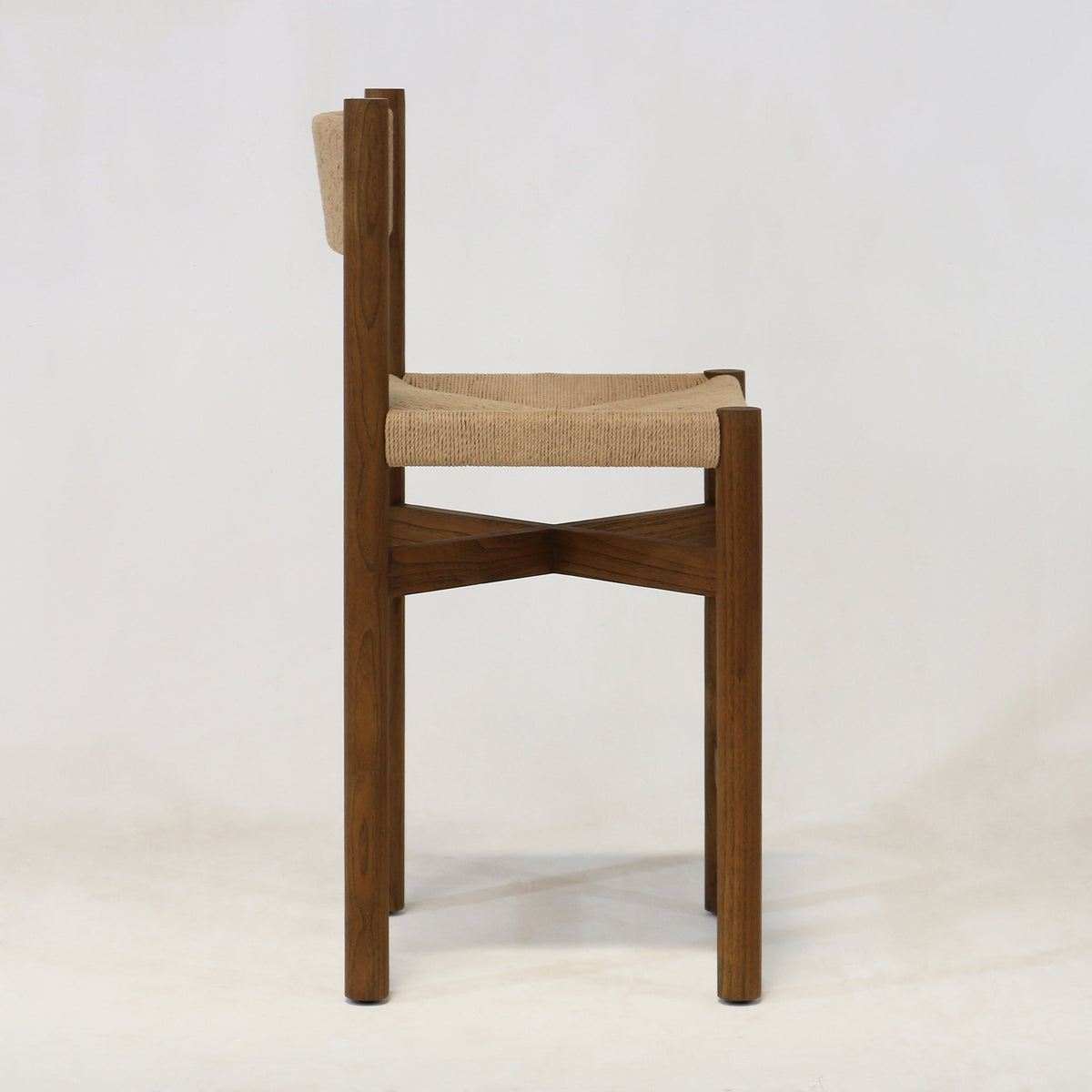 Side profile of a walnut wood counter stool with a natural woven papercord seat and low back, slim square legs and X-shaped stretcher shown on a plain white background.
