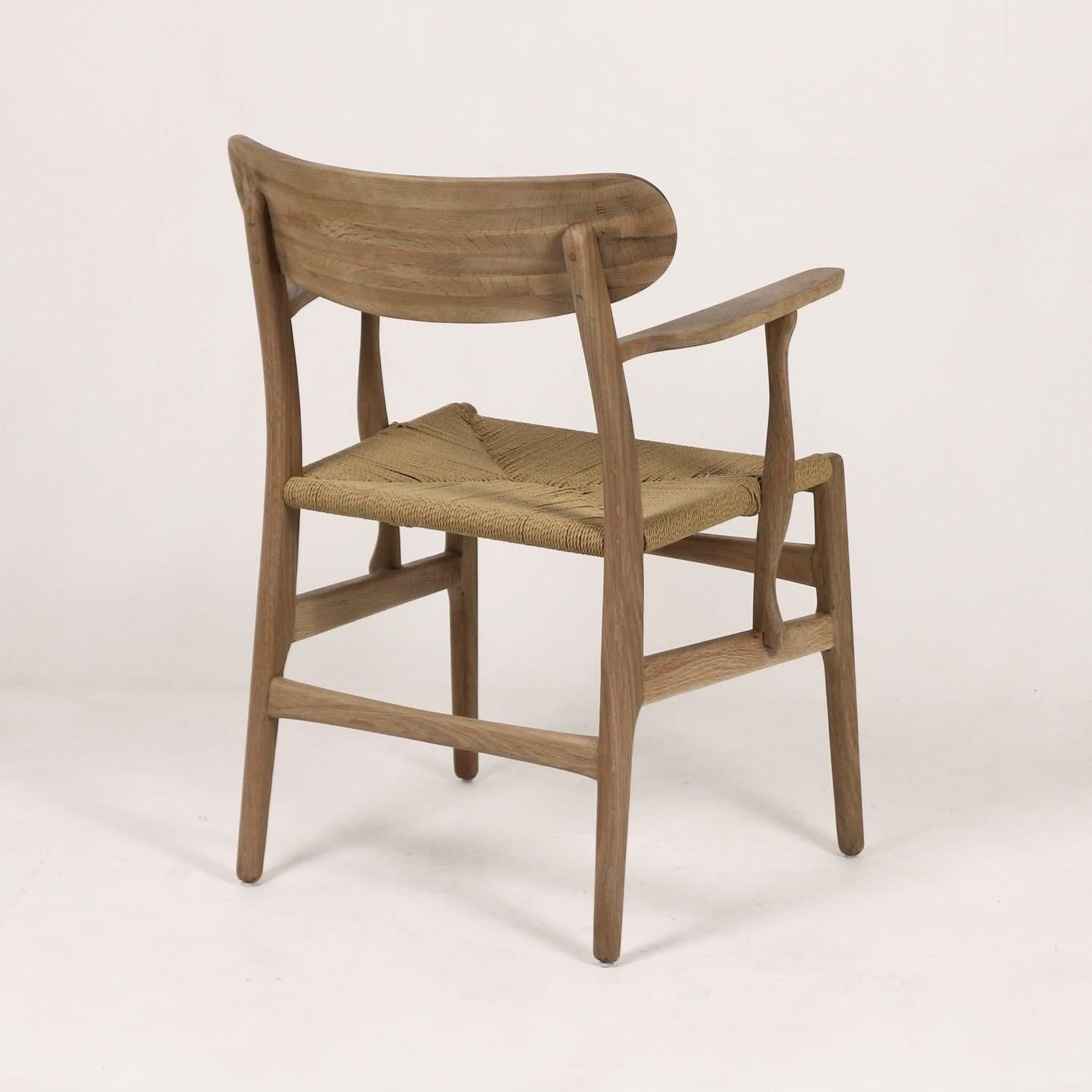 Rear three-quarter view of a modern Scandinavian solid wood dining chair with a light natural finish, curved back and arms, and a woven rope seat.
