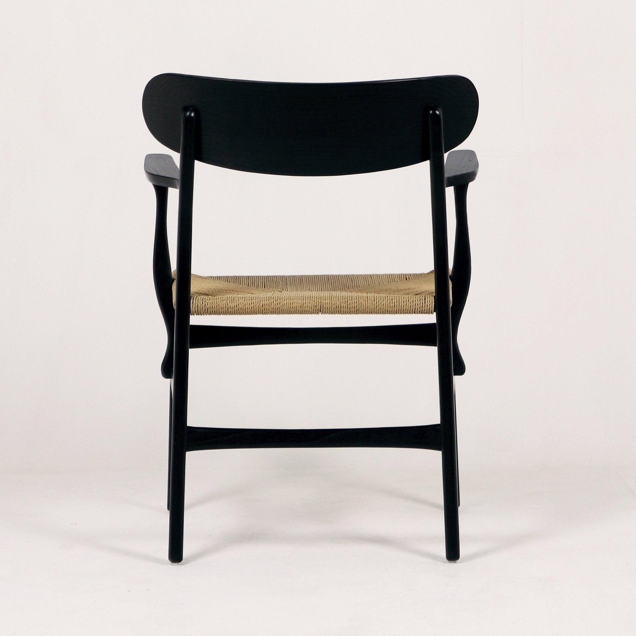 Rear view of a black solid wood accent dining chair with a curved backrest, sculpted arms and a natural woven rope seat shown against a plain white background.