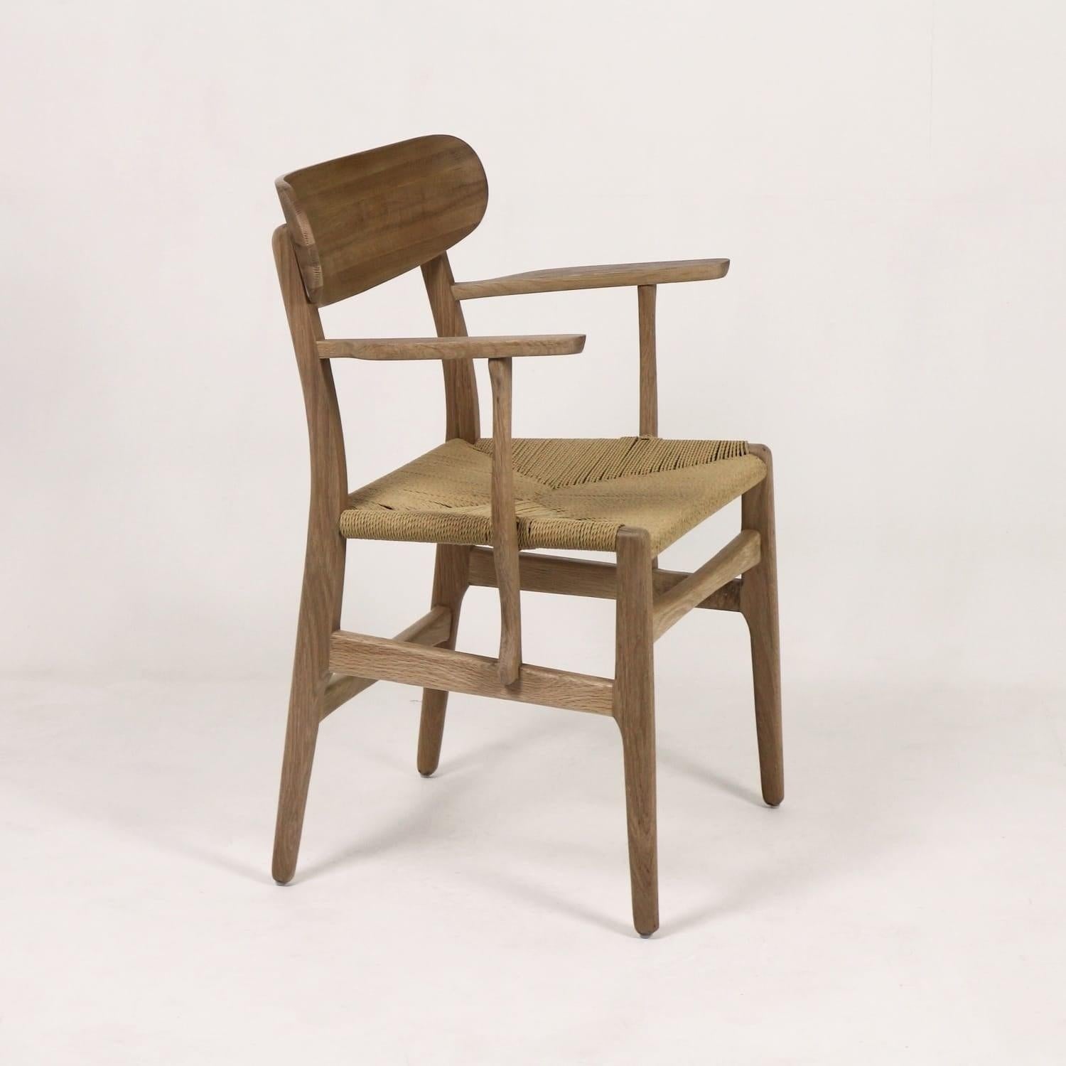 Side view of a Scandinavian-style solid wood dining armchair with a curved wooden backrest, slender tapered legs and a woven natural rope seat in a light brown oak finish.