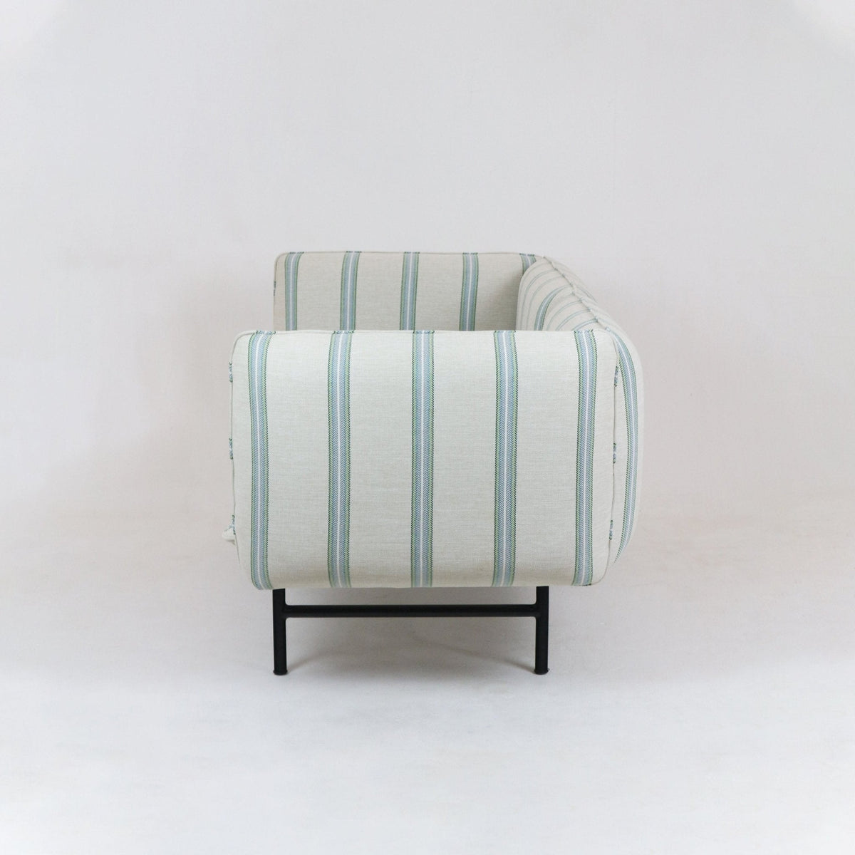 Side view of an outdoor sectional sofa upholstered in light neutral fabric with vertical green-blue stripes, featuring low black metal legs and rounded arm and back against a plain white background.
