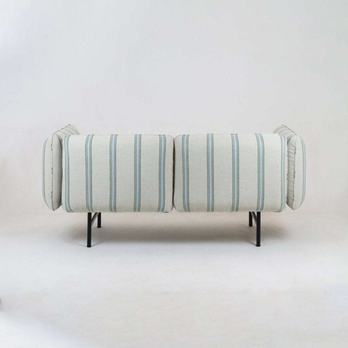 Back view of a modern coastal outdoor sectional upholstered in light neutral fabric with pale green-blue vertical stripes, supported on slim black metal legs.