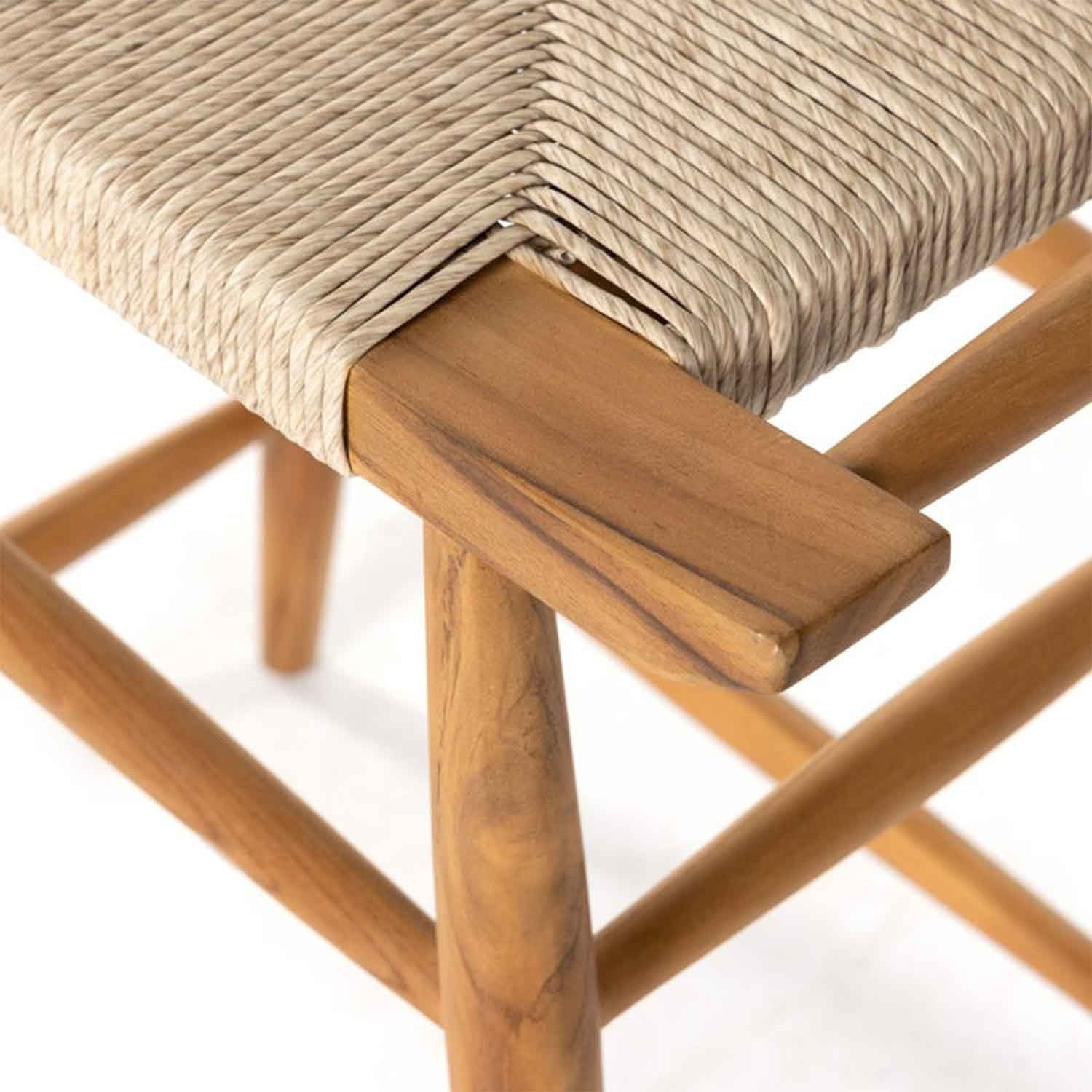 Close-up of a teak outdoor bar stool corner showing natural teak wood legs and stretcher with a tightly woven beige natural-fiber seat, highlighting wood grain and handwoven rope texture.