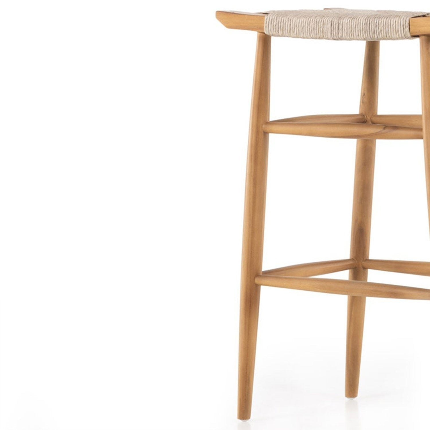 Close-up of the right side of a backless natural teak outdoor bar stool showing tapered legs, rounded footrest rails and a woven natural-fiber seat edge in a coastal Scandinavian style.