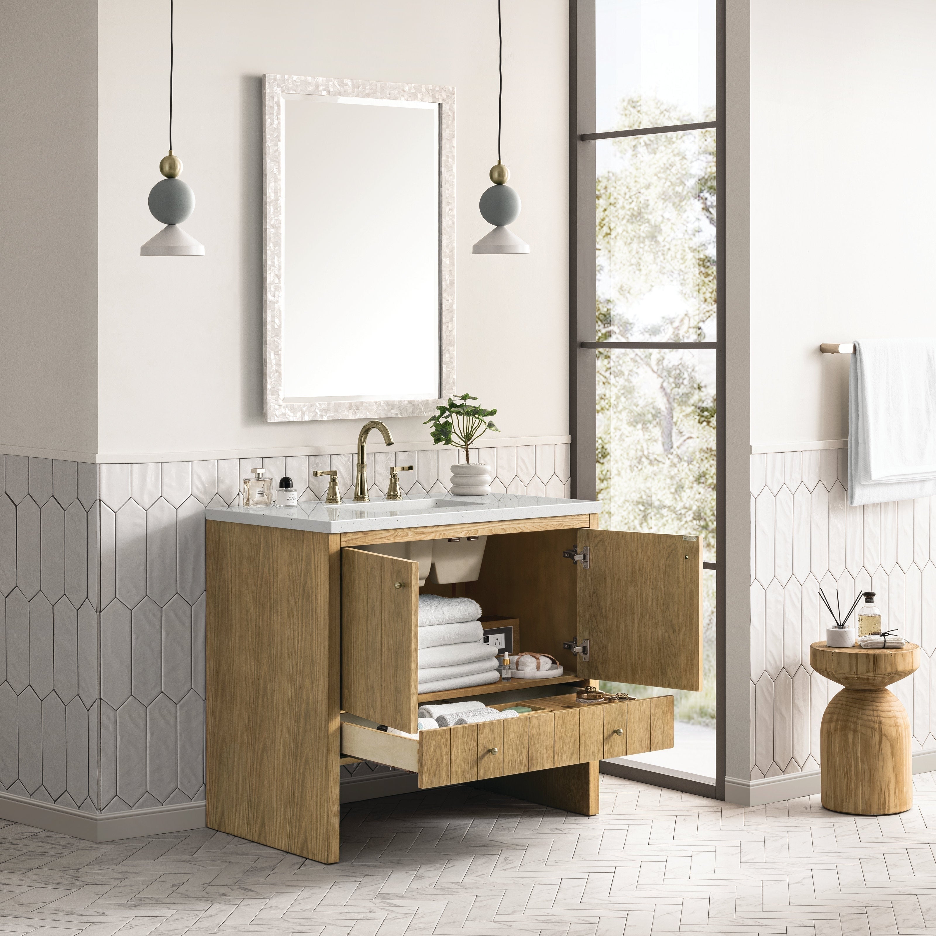 A modern bathroom features the NUEMA Sala 36 Single Bathroom Vanity with open cabinet doors and drawer displaying stacked towels and toiletries, complemented by a large mirror, stone countertop, pendant lights, and natural light.