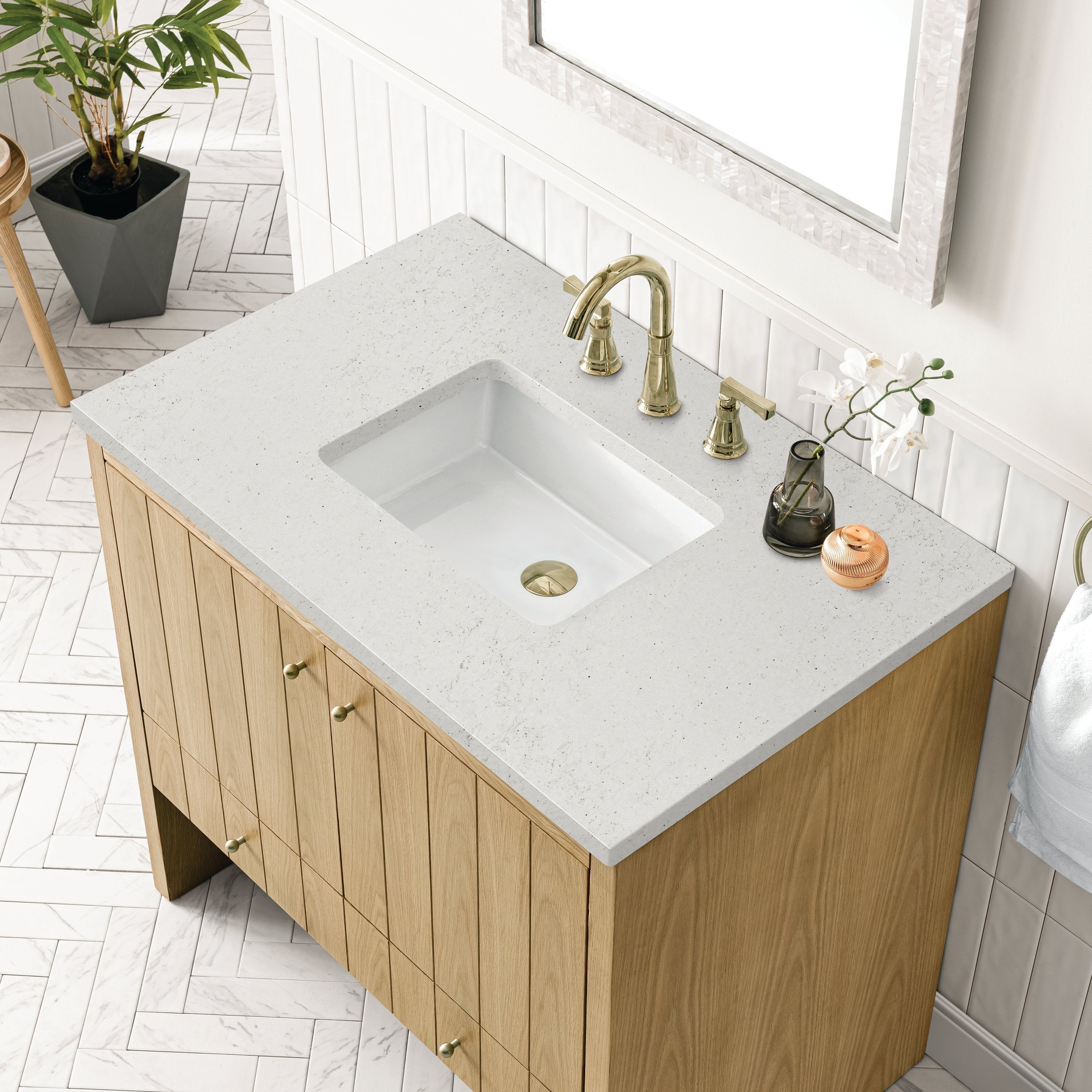 The NUEMA Sala 36 Single Bathroom Vanity features a modern solid oak cabinet, white rectangular sink, brass faucet, small vase with white flowers, soap dispenser, round container on a stone countertop, and herringbone tile flooring.