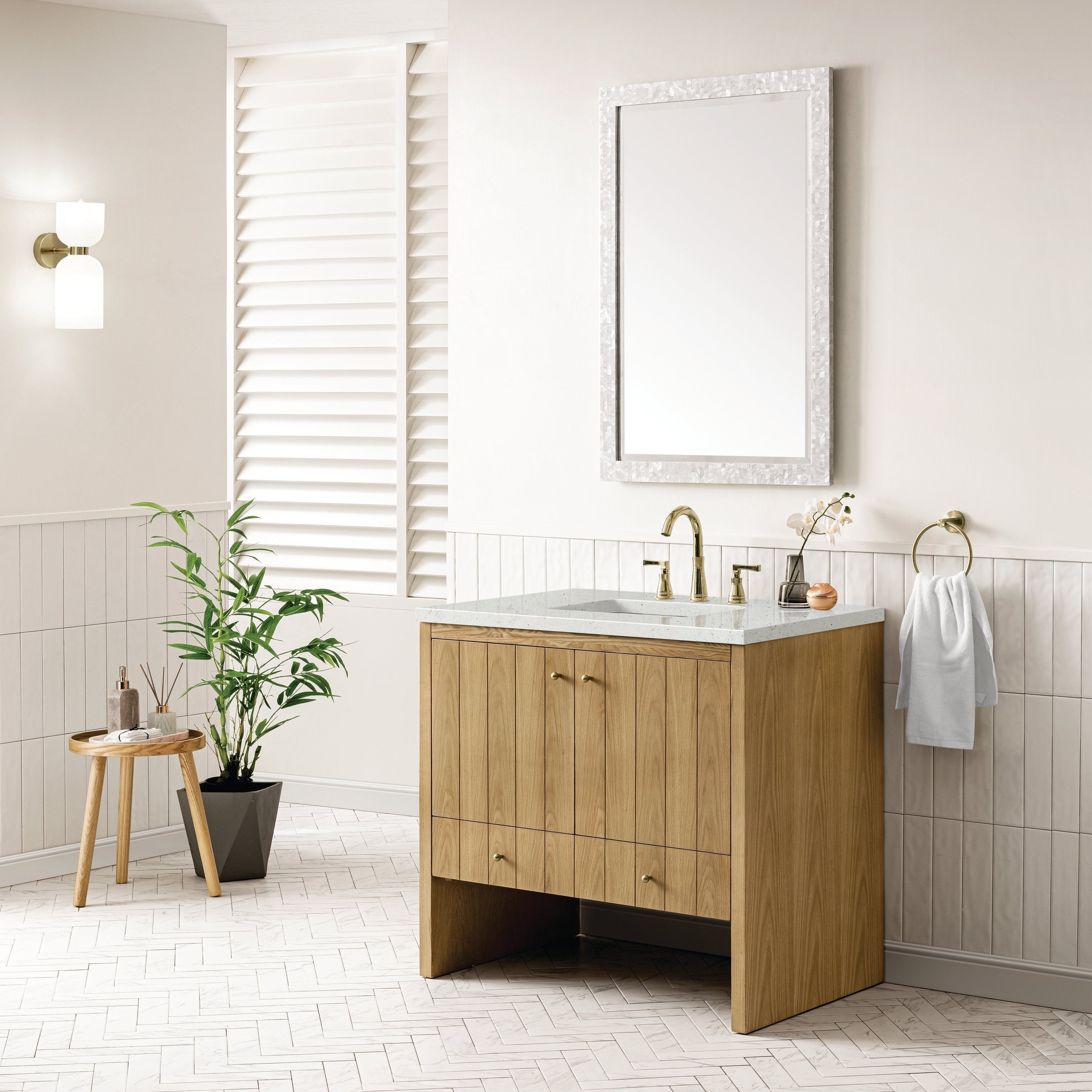 A modern bathroom features the NUEMA Sala 36 Single Bathroom Vanity with a marble countertop and brass faucet. Above, a rectangular mirror with a textured white frame hangs over light walls with white tile accents.