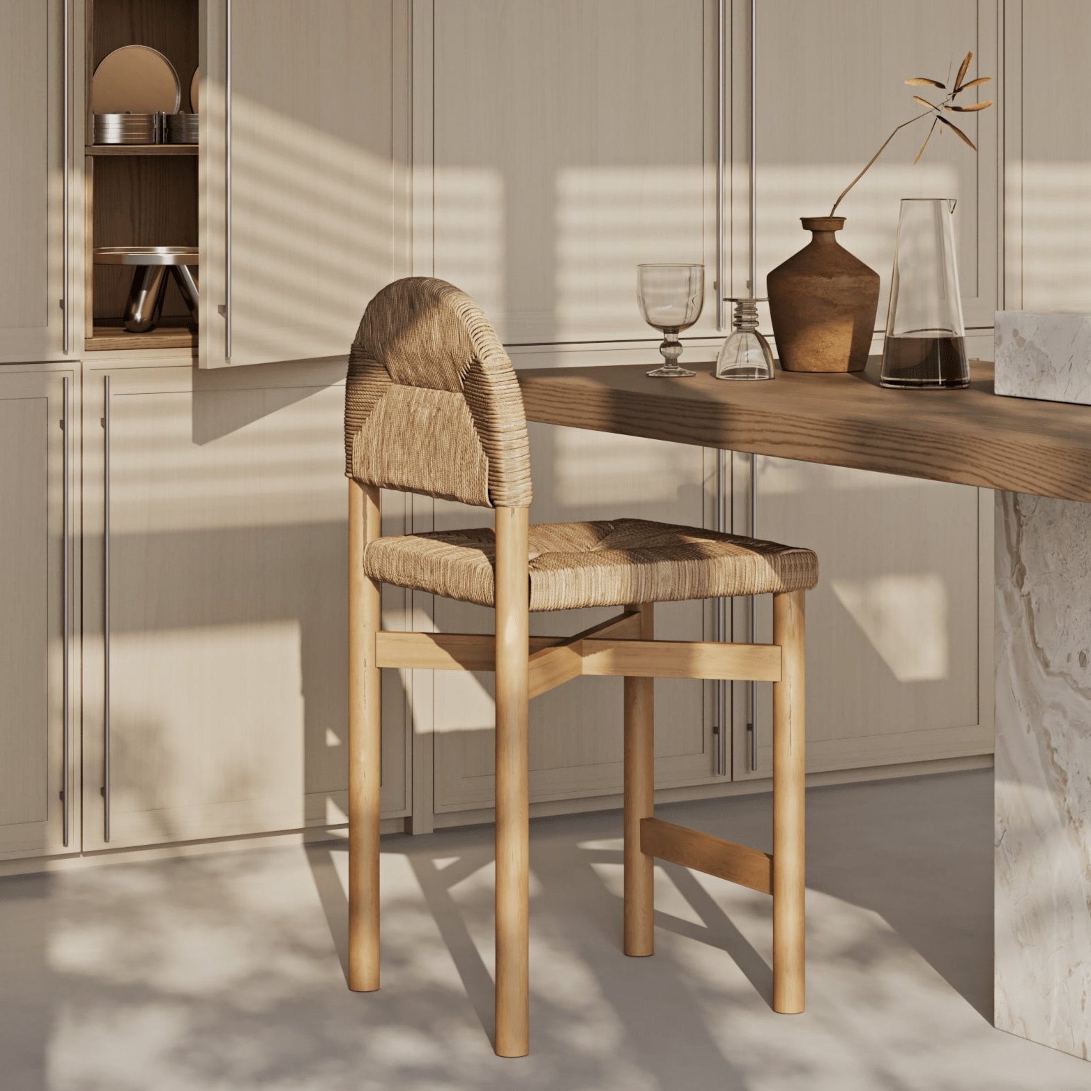 Natural teak counter stool with woven seagrass seat and rounded woven back, placed at a wood kitchen island in warm coastal tones with sunlight highlighting the wood grain and woven texture.