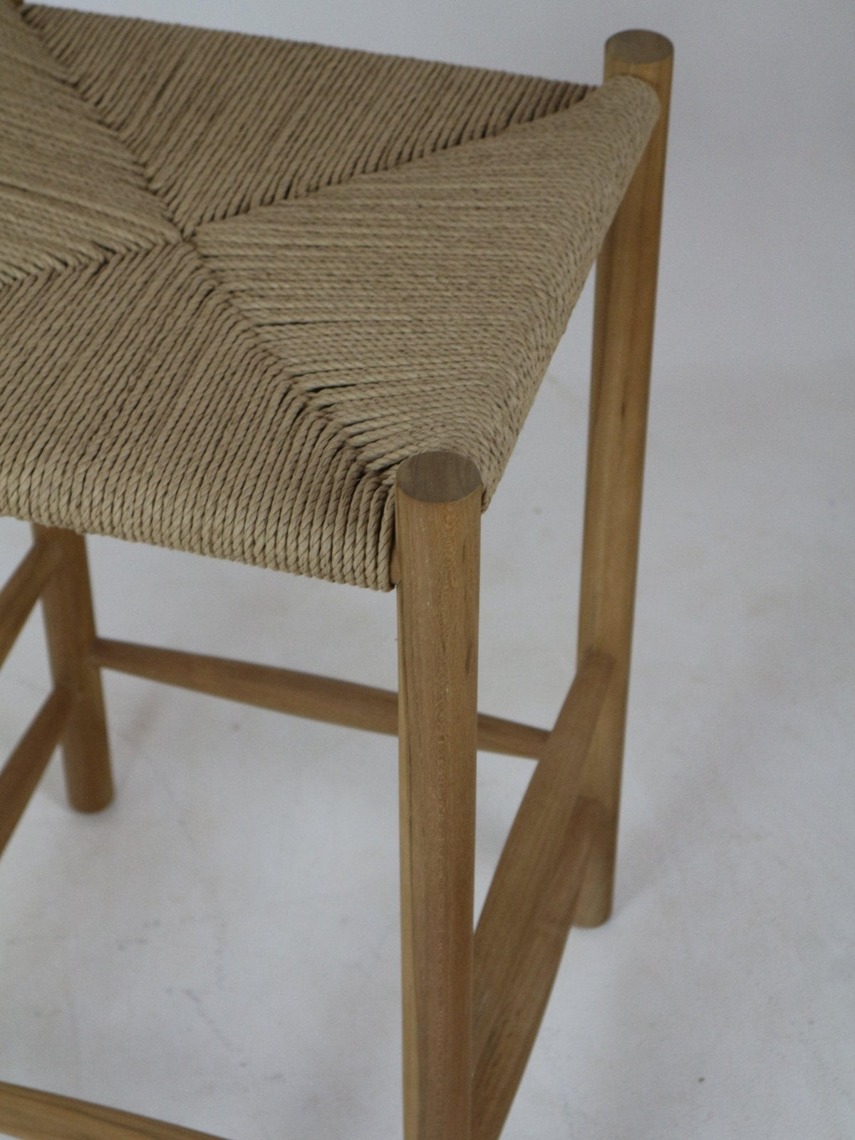 Close-up of a modern natural wood bar stool showing a beige woven rope seat corner and round natural wood legs with stretcher rails.