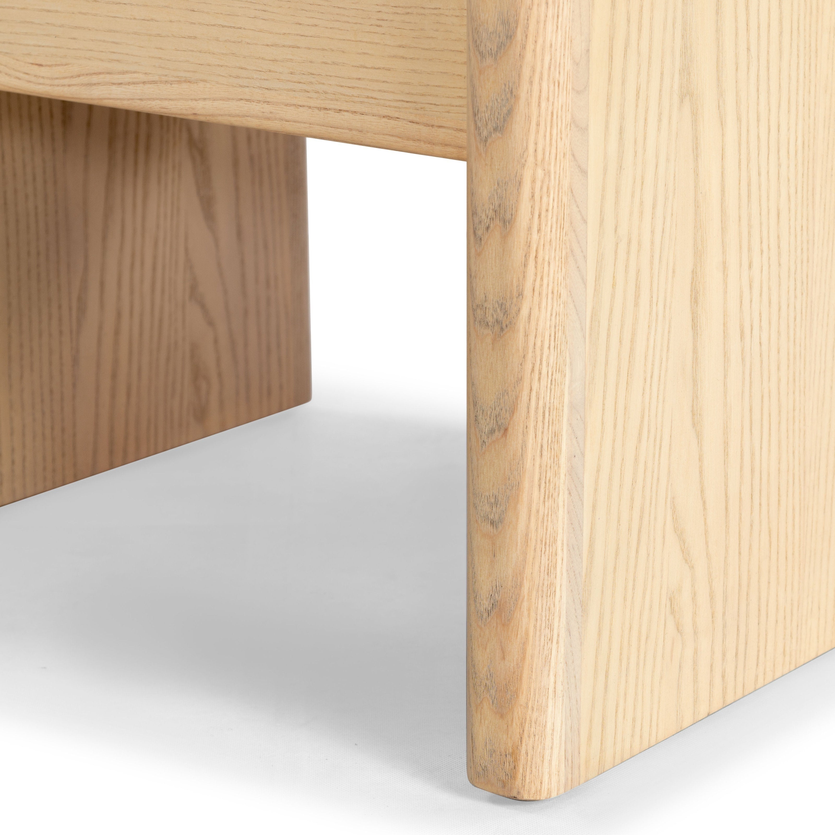 Close-up of a nightstand's natural wood leg and lower apron showing a light finish, pronounced wood grain and a rounded corner in a modern minimalist style.